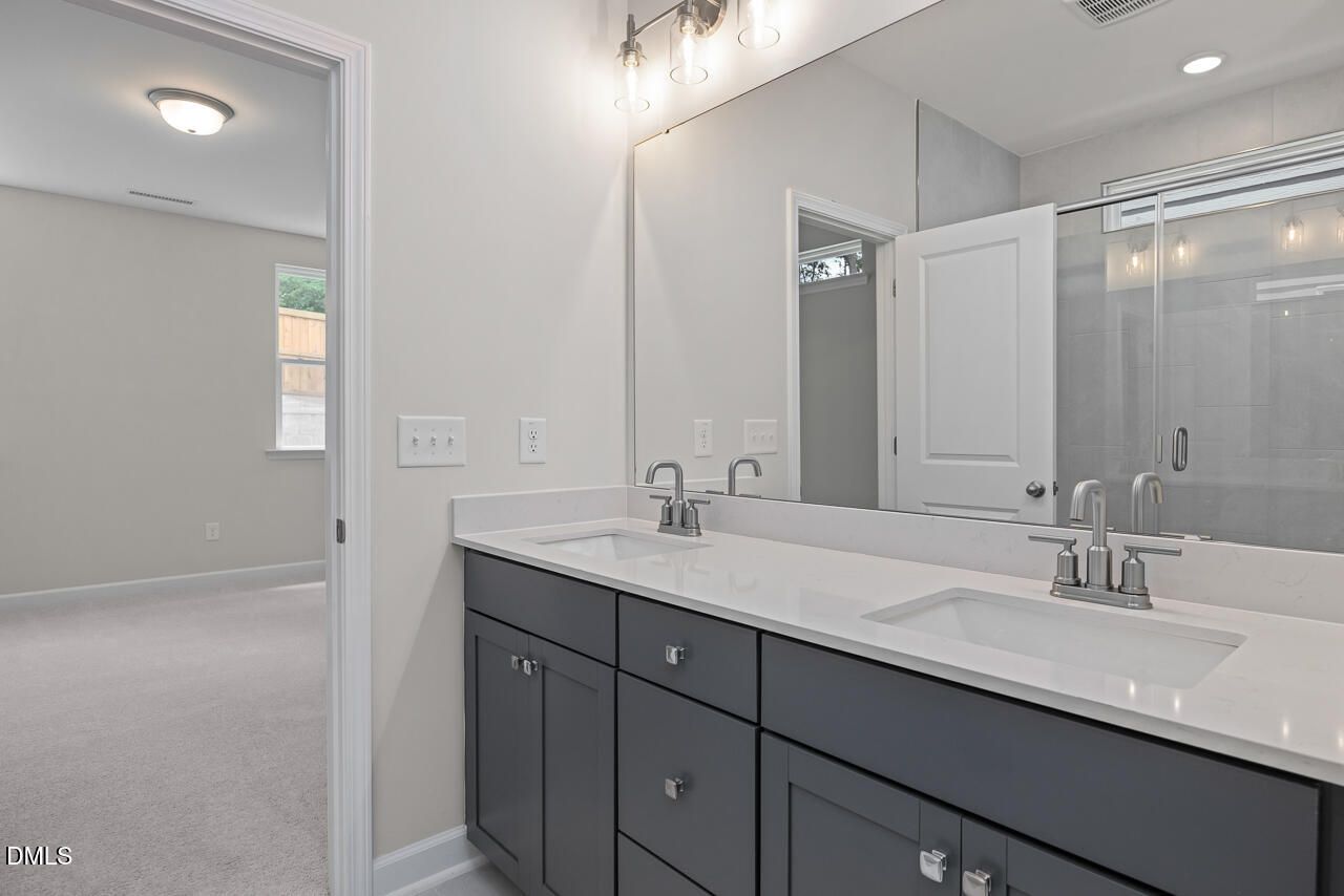 Modern primary bathroom with double vanity and glass-enclosed shower in The Ashport G, Sage on North Main, Wake Forest.
