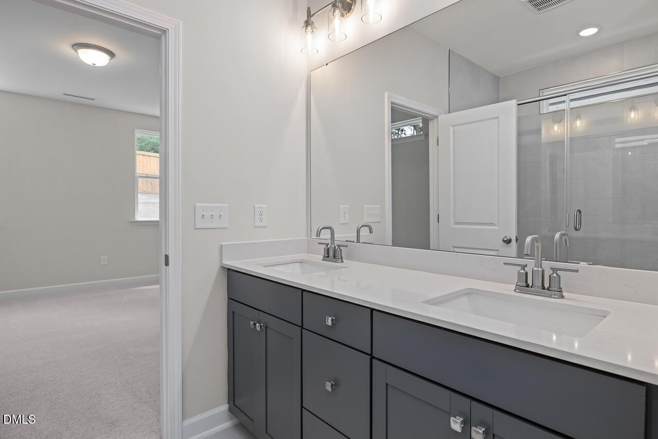 Modern primary bathroom with double vanity and glass-enclosed shower in The Ashport G, Sage on North Main, Wake Forest.