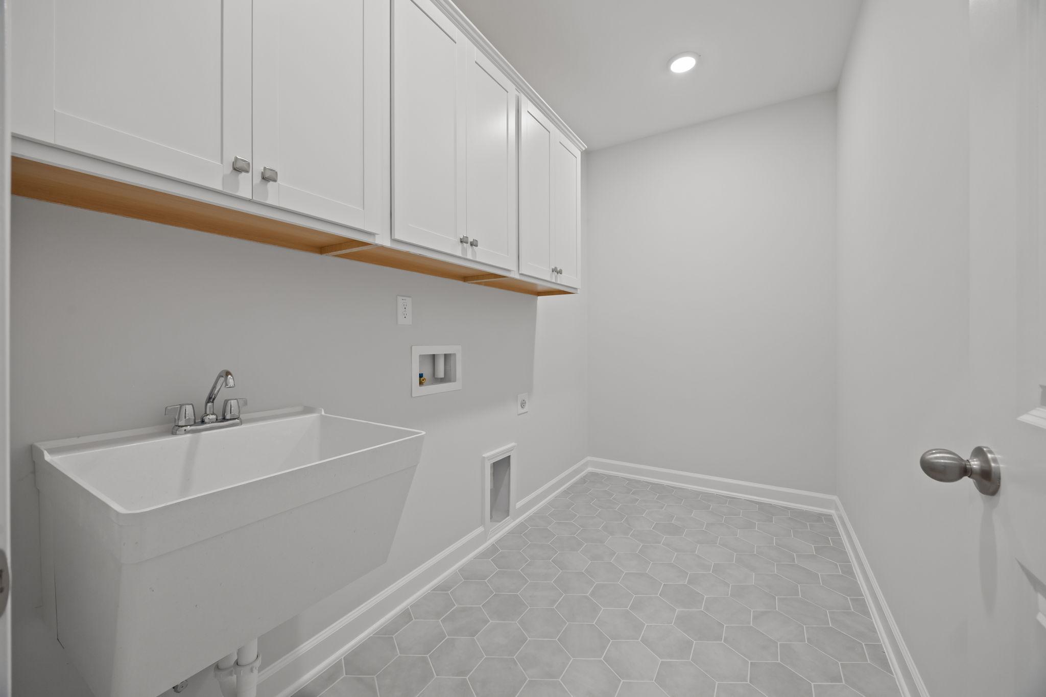 Laundry room in The Ashport B featuring white cabinetry, utility sink, and grey hexagonal tile flooring.