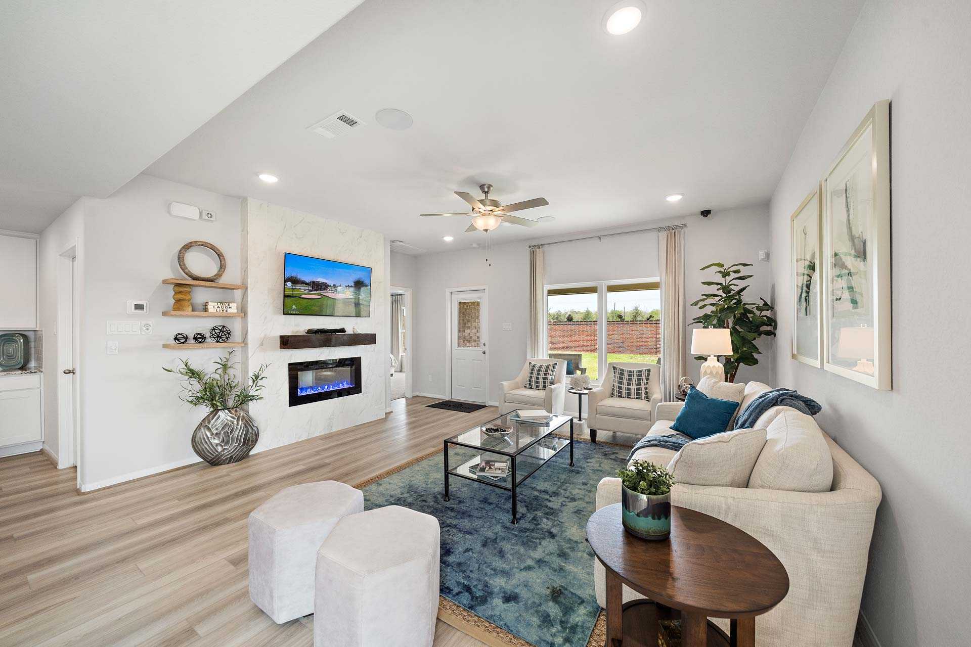 Open-concept living room in Sunterra Katy Texas with hardwood floors gas fireplace TV wall beige sofa and large windows