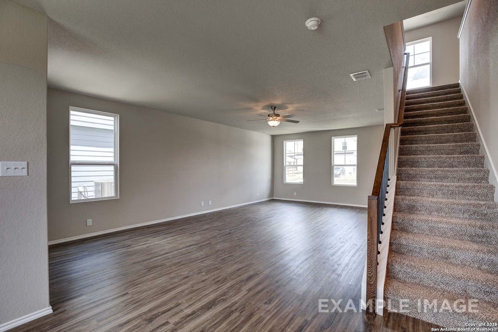 Spacious two-story entry with beige walls, hardwood floors, large windows, ceiling fan, and carpeted staircase in Davidson Homes The Murray K, San Antonio