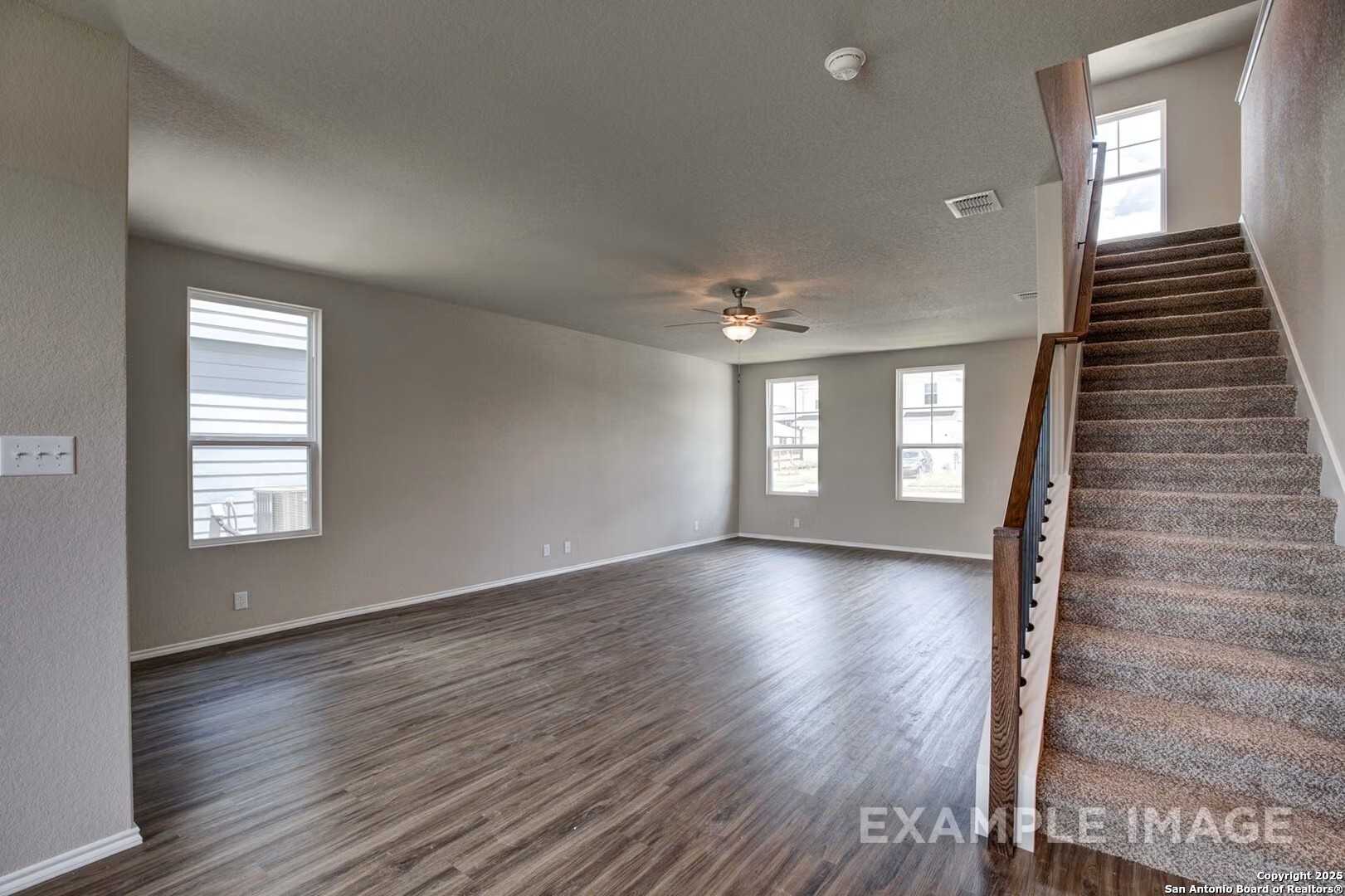Spacious two-story entry with beige walls, hardwood floors, large windows, ceiling fan, and carpeted staircase in Davidson Homes The Murray K, San Antonio