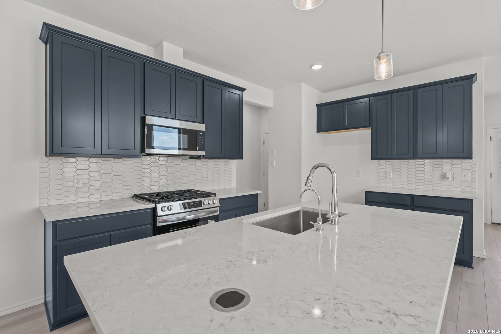 Modern kitchen with navy cabinets, quartz island, and stainless appliances in The Gillian C home, Meadows at Oak Creek.