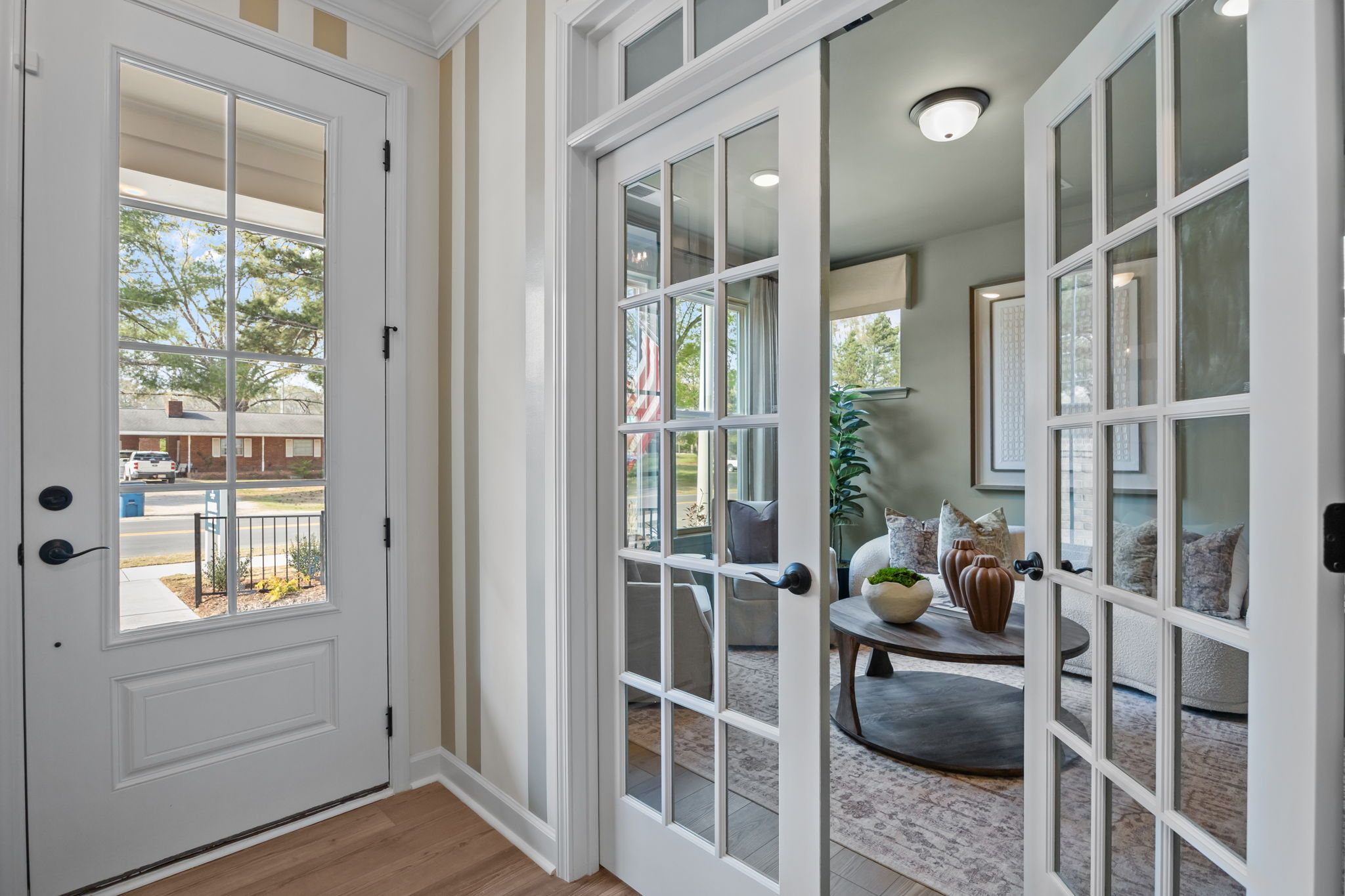 Inviting entryway with open French doors to modern living room, white sofas, plants at Camden Park, Knightdale NC by Davidson Homes