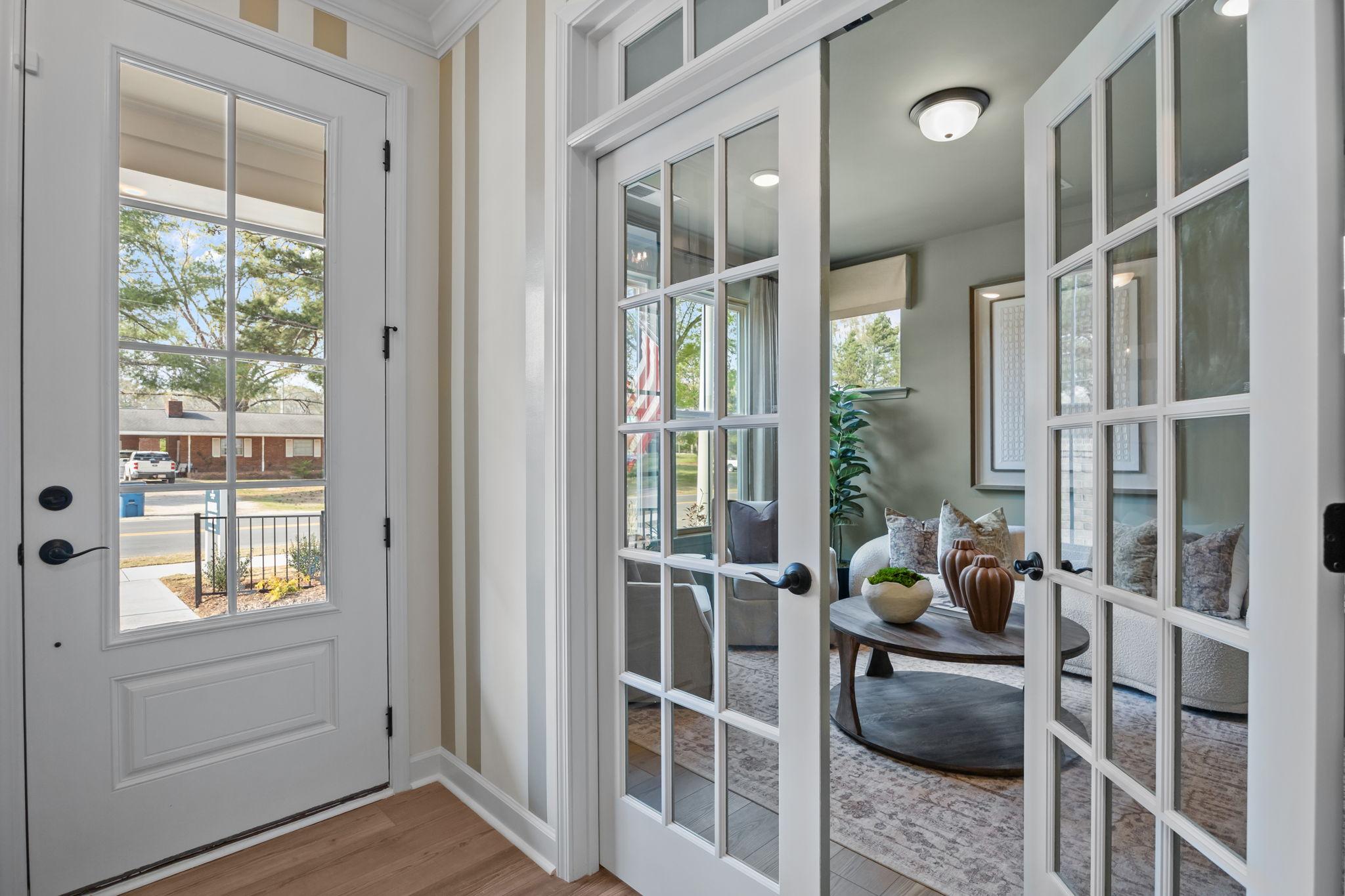 Inviting entryway with open French doors to modern living room, white sofas, plants at Camden Park, Knightdale NC by Davidson Homes