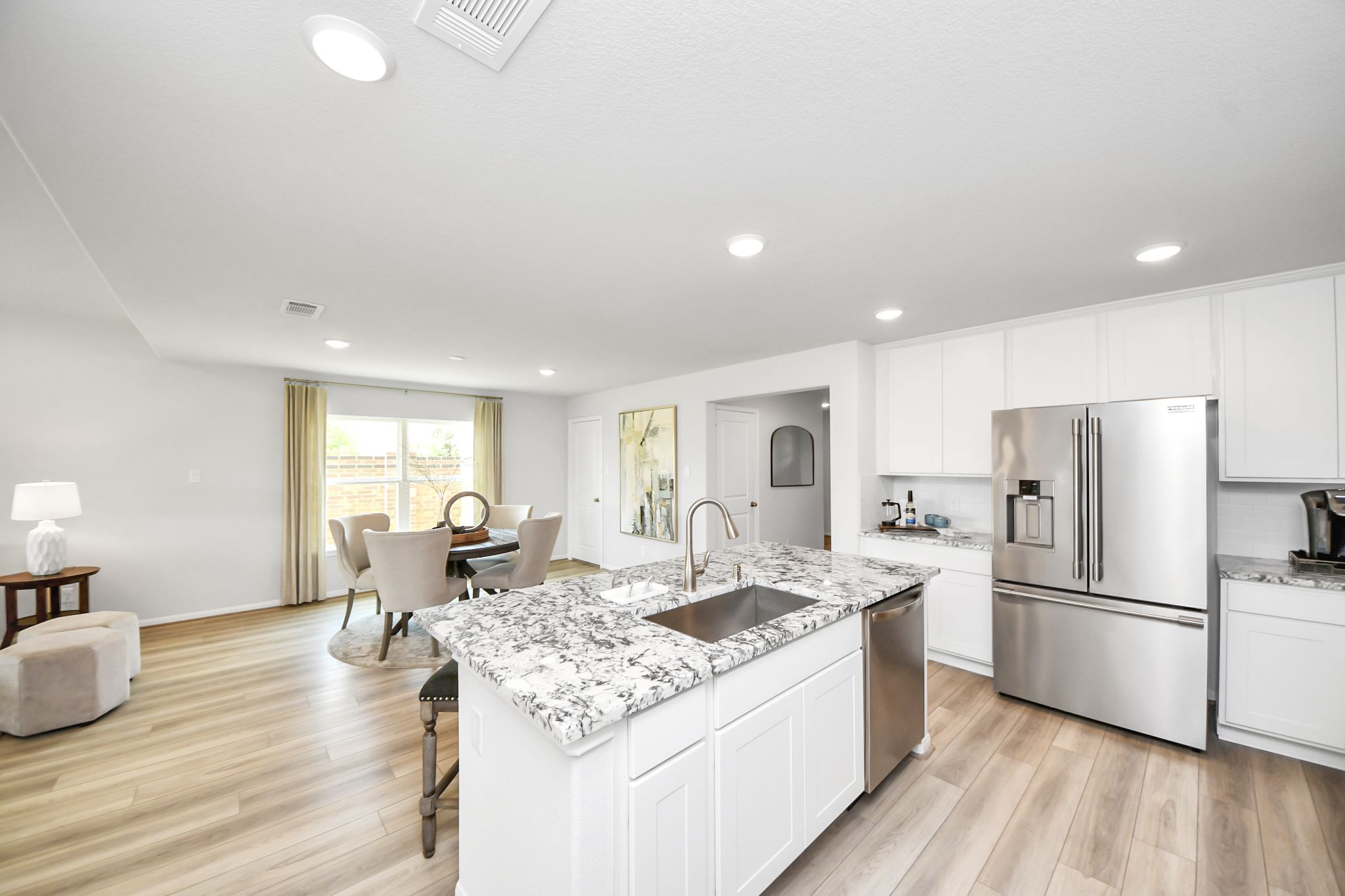Open-concept kitchen and dining area at Sunterra in Katy, TX, by Davidson Homes featuring granite island and white cabinets.