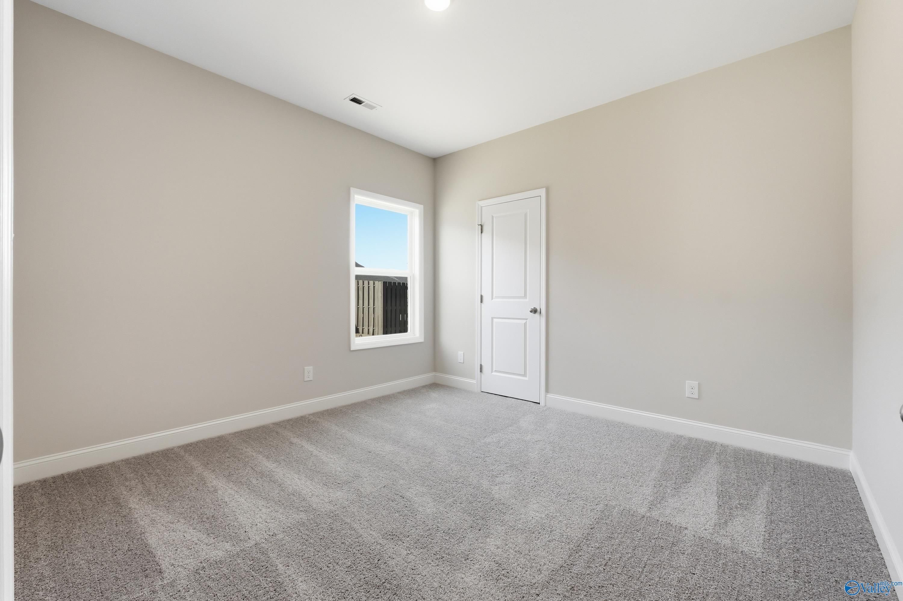 Empty secondary bedroom with beige walls, gray carpet, window overlooking blue sky in Davidson Homes The Everett, Harvest, AL
