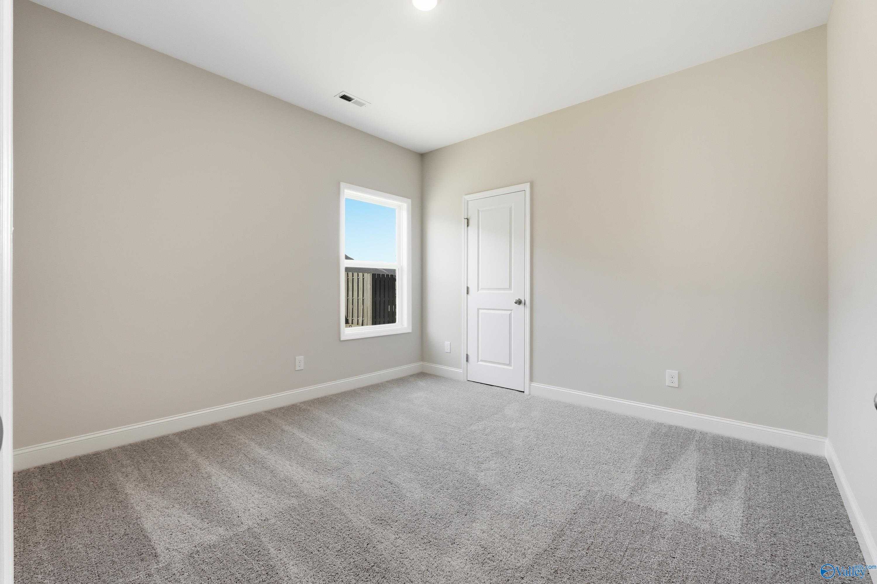 Empty secondary bedroom with beige walls, gray carpet, window overlooking blue sky in Davidson Homes The Everett, Harvest, AL