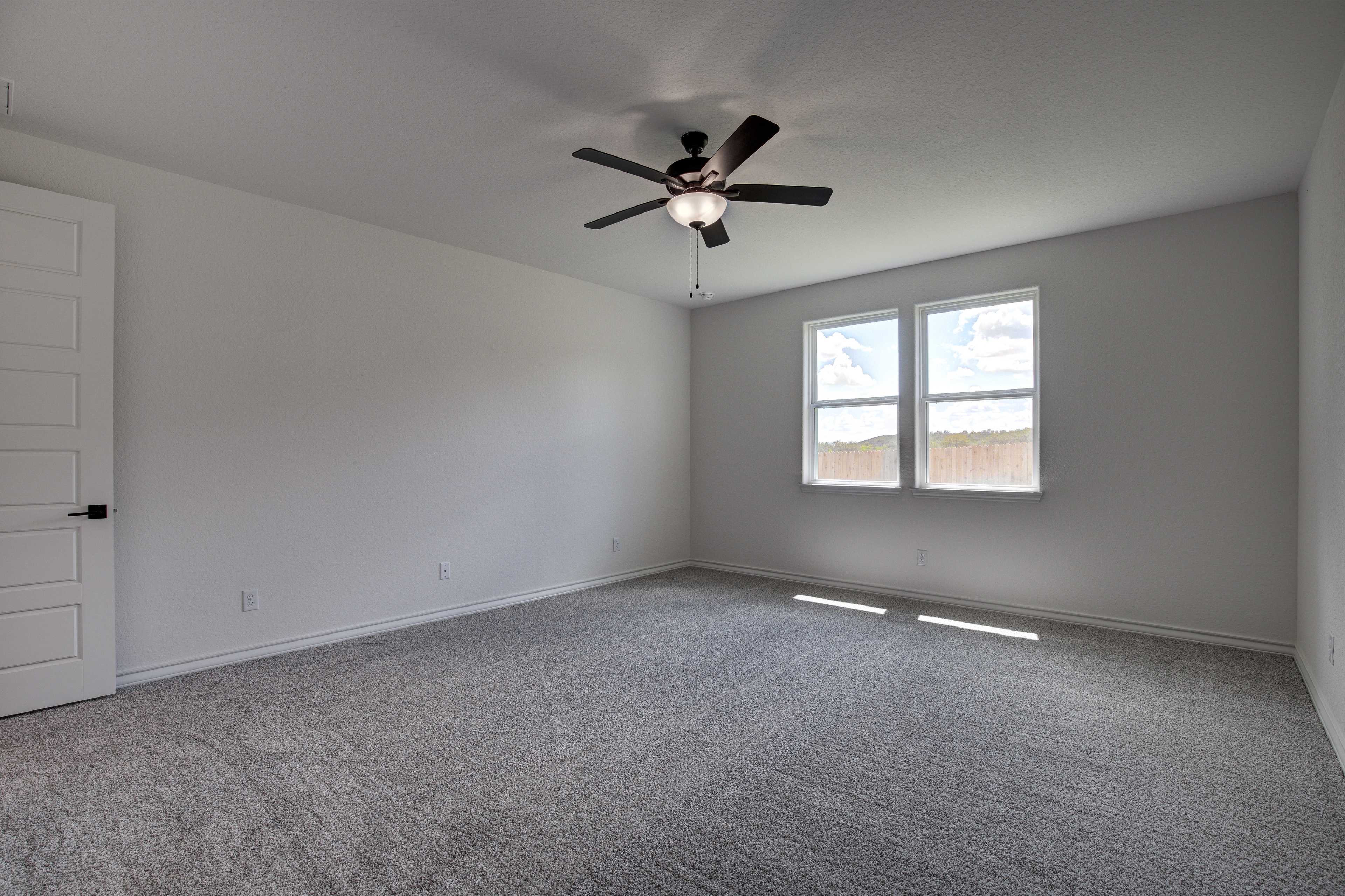Spacious master bedroom in The Lanier home with gray carpet, ceiling fan, white walls, and sunlit double windows