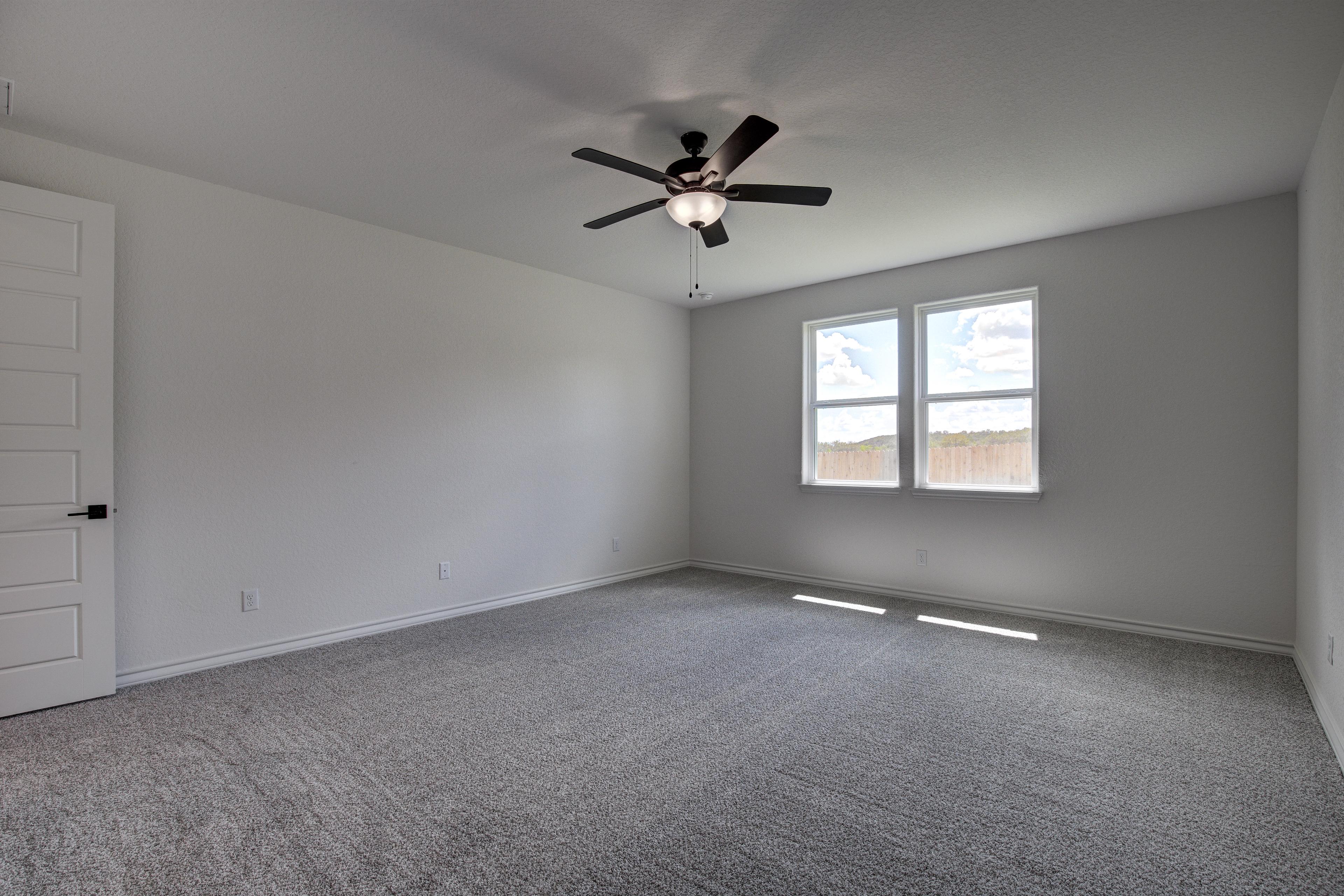 Spacious master bedroom in The Lanier floor plan with ceiling fan, large windows, gray carpet, and white walls