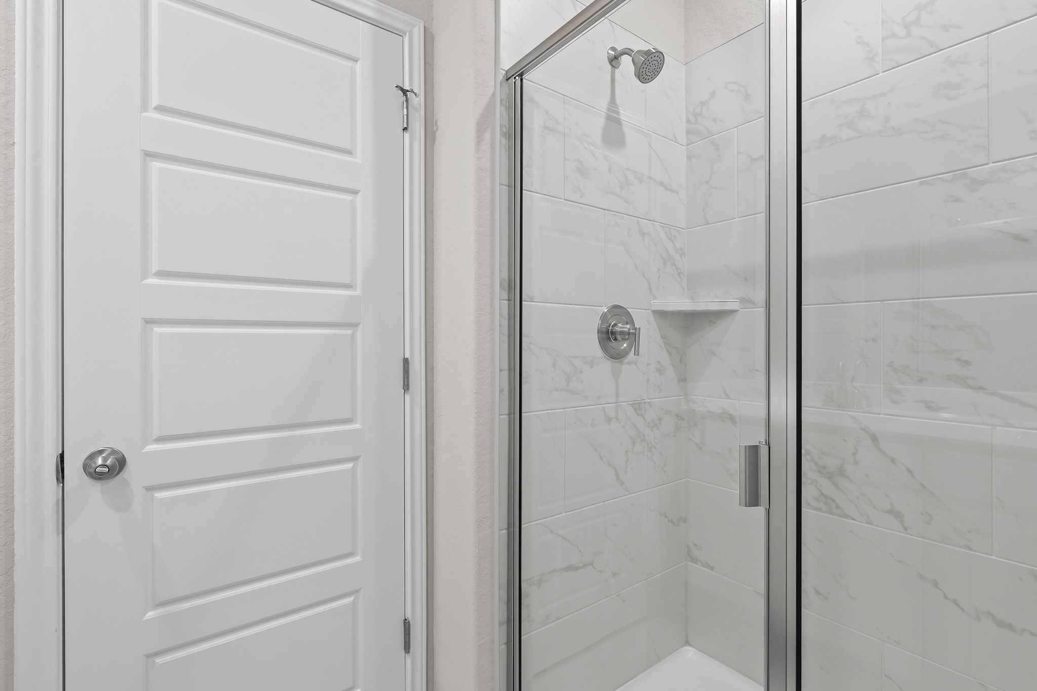 Modern walk-in shower with white marble-style tile in the master suite of The Colorado B home design.