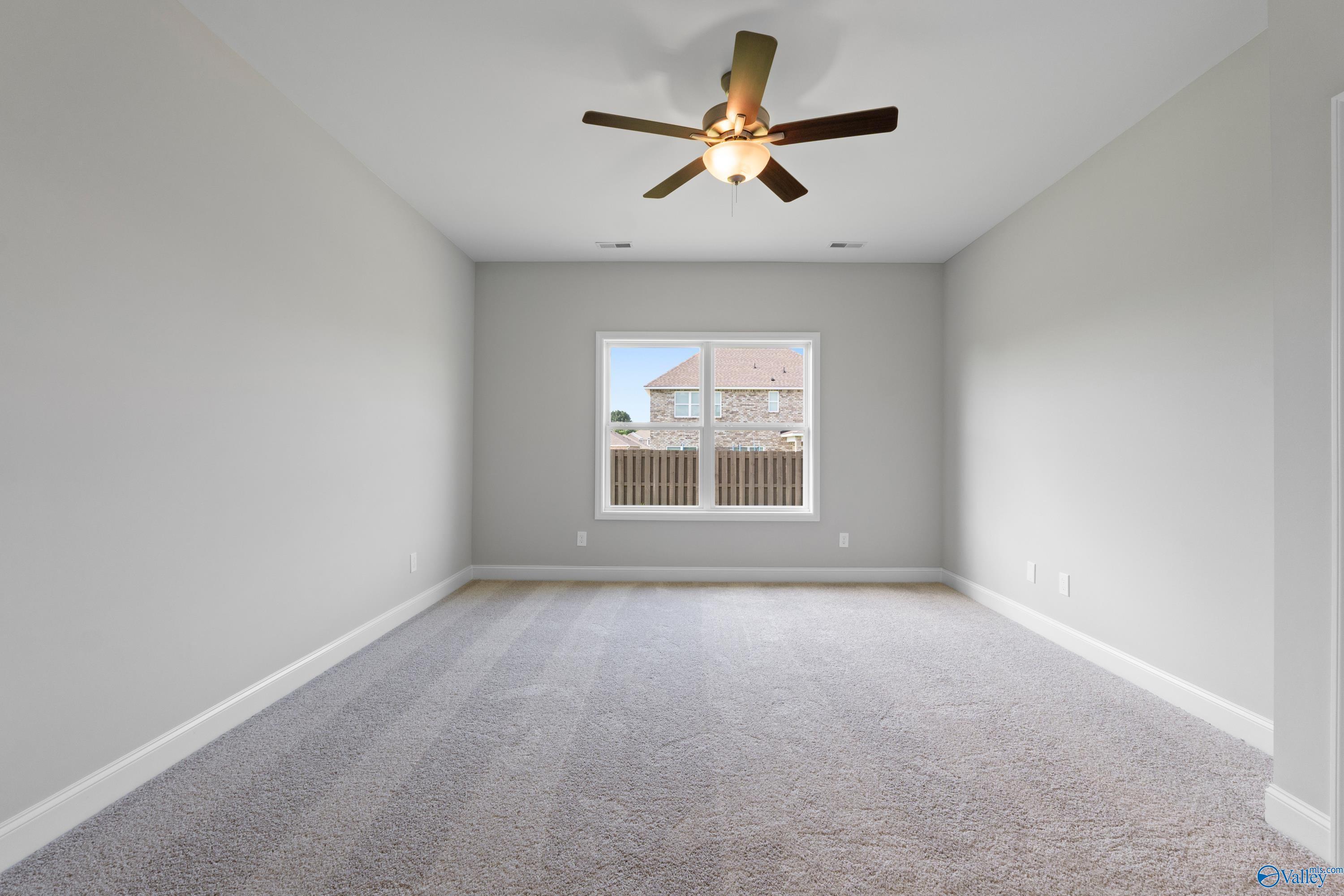 Empty secondary bedroom featuring ceiling fan, large window with blinds, neutral gray walls and carpet in Davidson Homes The Everett B, Toney, Alabama