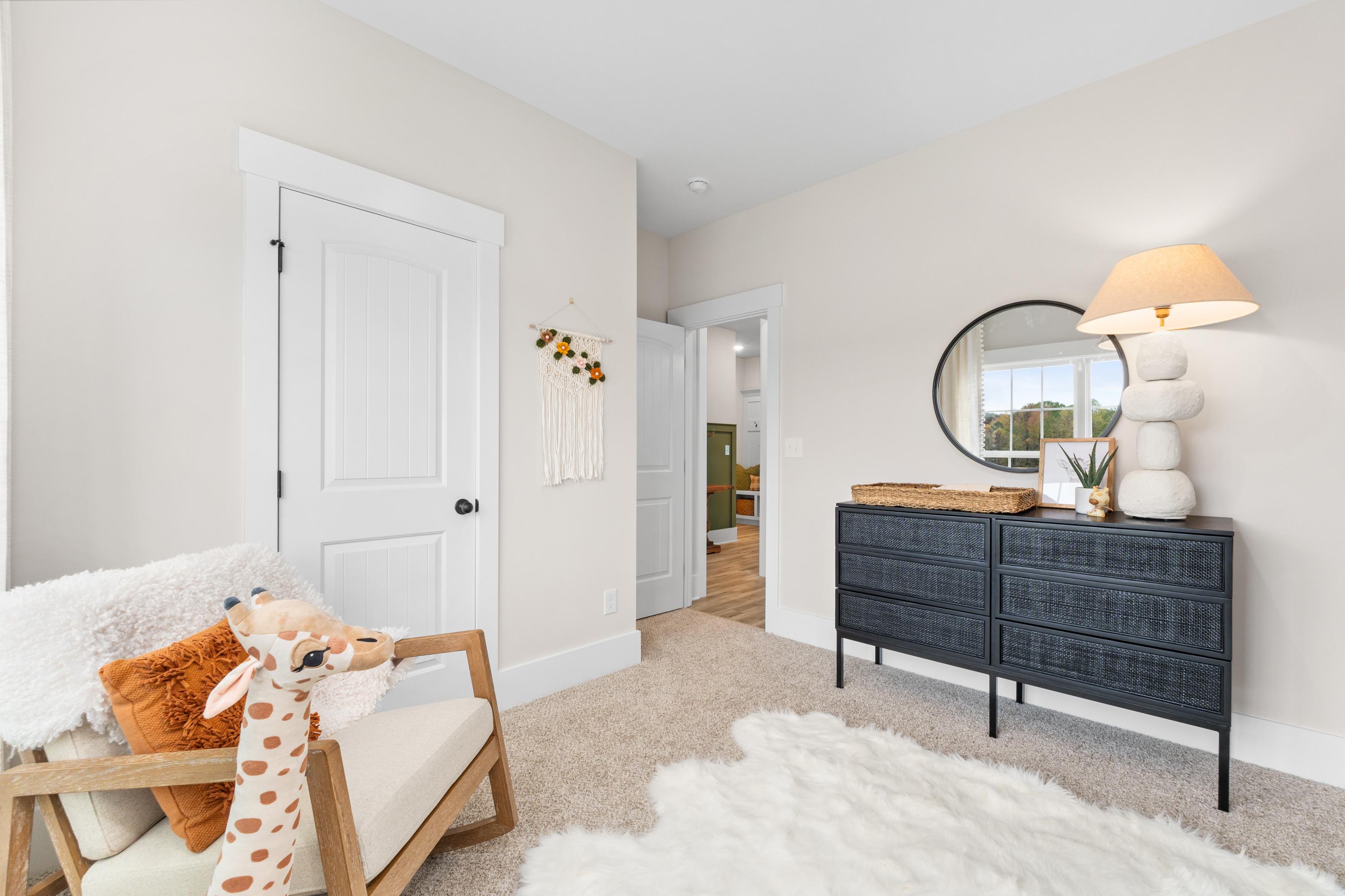 Cozy nursery bedroom at Spragins Cove in Huntsville Alabama with giraffe plush on armchair, black rattan dresser, round mirror
