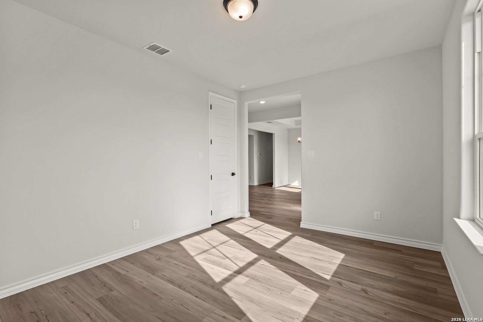 Bright empty bedroom with wood-look flooring and natural light in Davidson Homes The Oxford F, Potranco Oaks, Castroville, Texas