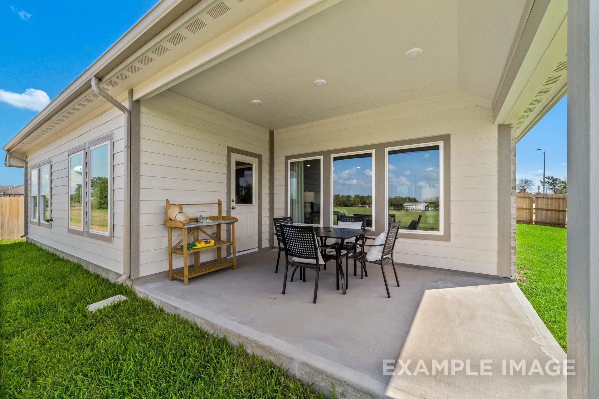 Covered back patio with dining table, chairs, and sideboard overlooking green lawn in Davidson Homes The Acadia A, Lago Mar, Texas City
