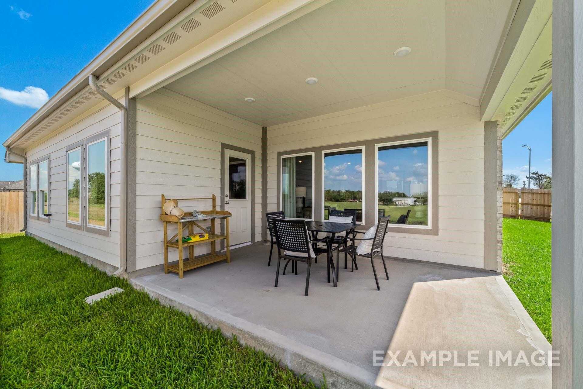 Covered back patio with dining table and chairs, large windows, and lush green lawn in Davidson Homes The Acadia A, Lago Mar, Texas City