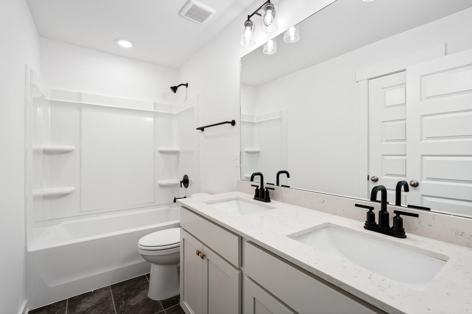 Modern bathroom with double vanity, quartz counters, black fixtures, tub, and glass shower in 5-bed Davidson Homes Ridgeport C, Gallatin, TN