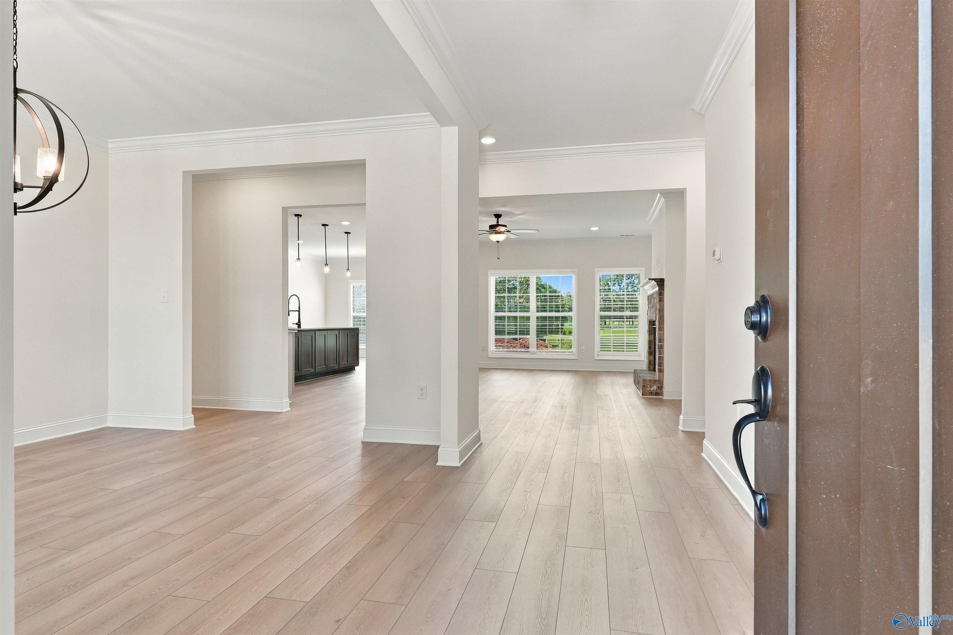 Foyer with light wood floors opening to great room with fireplace and kitchen at Davidson Homes The Valencia in Huntsville, Alabama