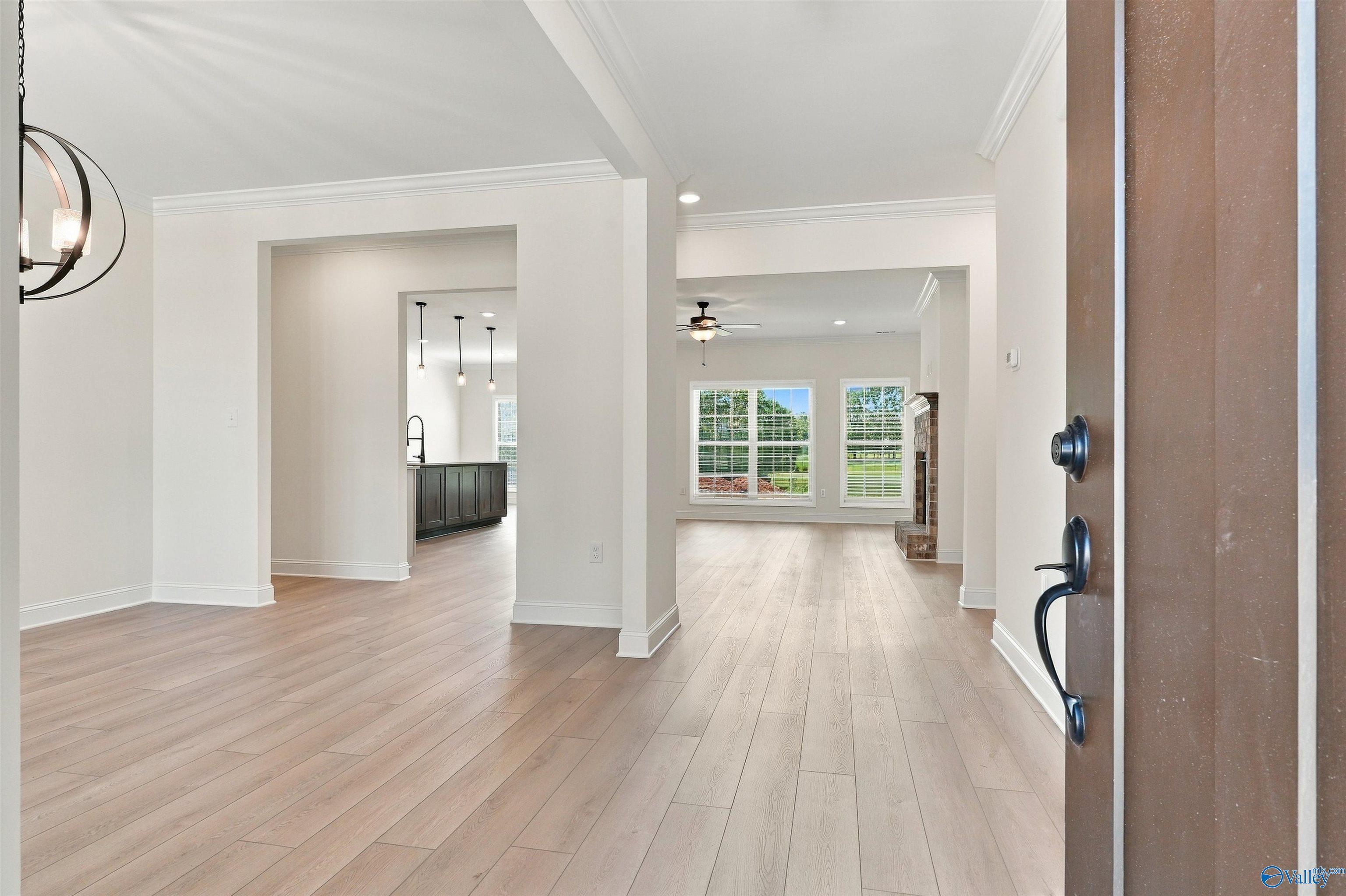 Foyer with light wood floors opening to great room with fireplace and kitchen at Davidson Homes The Valencia in Huntsville, Alabama