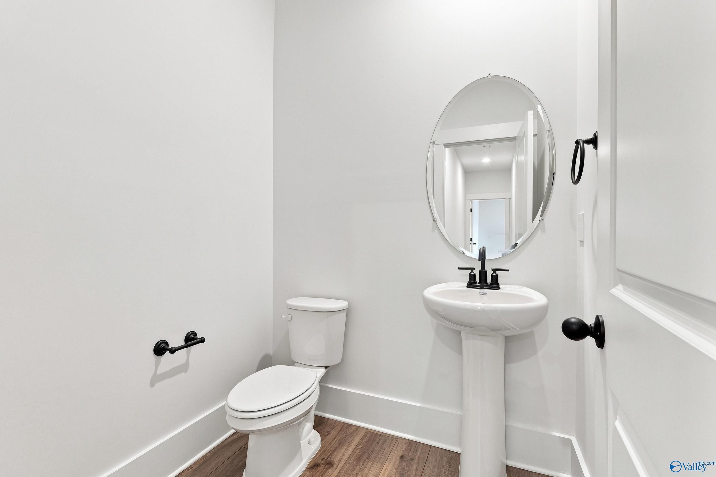 Elegant white half bath with pedestal sink, oval mirror, and matte black fixtures in Davidson Homes The Valencia, Huntsville
