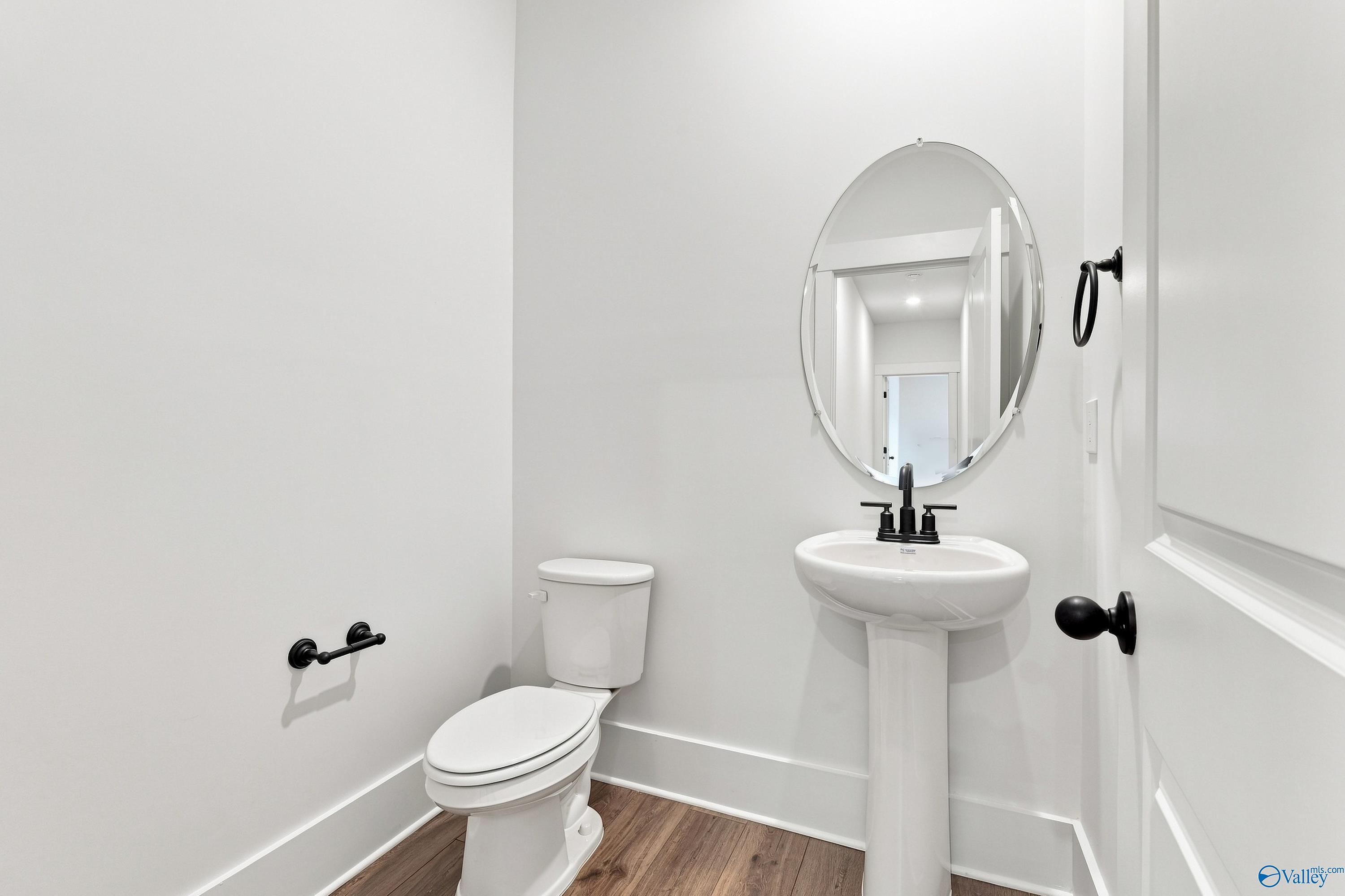 Elegant white half bath with pedestal sink, oval mirror, and matte black fixtures in Davidson Homes The Valencia, Huntsville