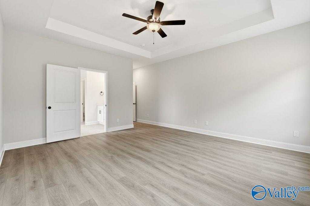 Spacious master bedroom with tray ceiling fan, light gray walls, hardwood floors, and open en-suite bath in Davidson Homes The Rockford B, Hartselle AL