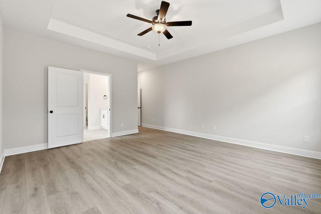 Spacious master bedroom with tray ceiling, ceiling fan, light gray walls, and open bathroom in Davidson Homes The Rockford B, Hartselle, Alabama