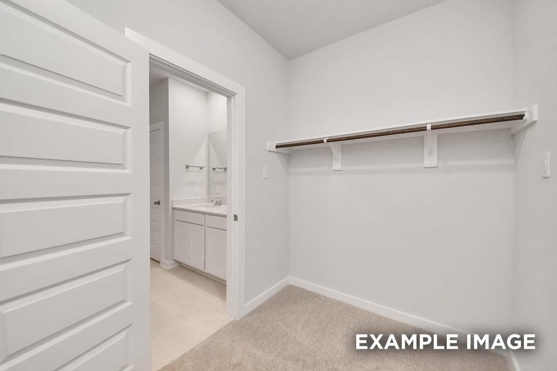 Spacious walk-in closet with hanging rod opening to master bath vanity in Davidson Homes The Blanco E, Magnolia, Texas