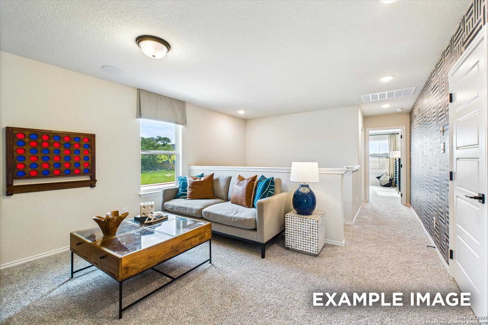 Cozy upstairs loft with gray sofa, glass-top coffee table, and window view of greenery in Davidson Homes The Florence C, San Antonio
