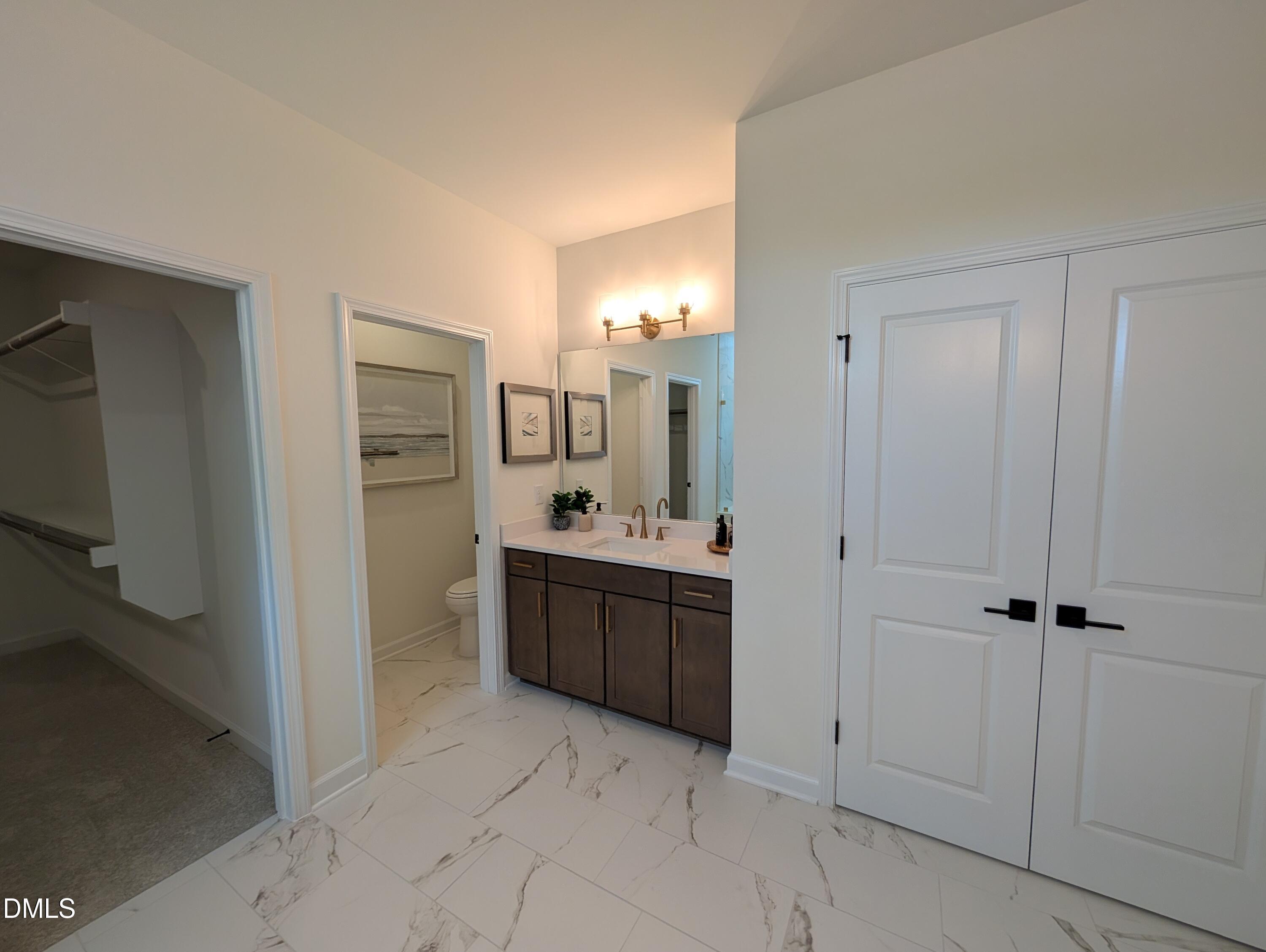 Modern bathroom vanity with dark wood cabinets, marble-style tile, and walk-in closet in The Aspen B at Wendell Ridge.