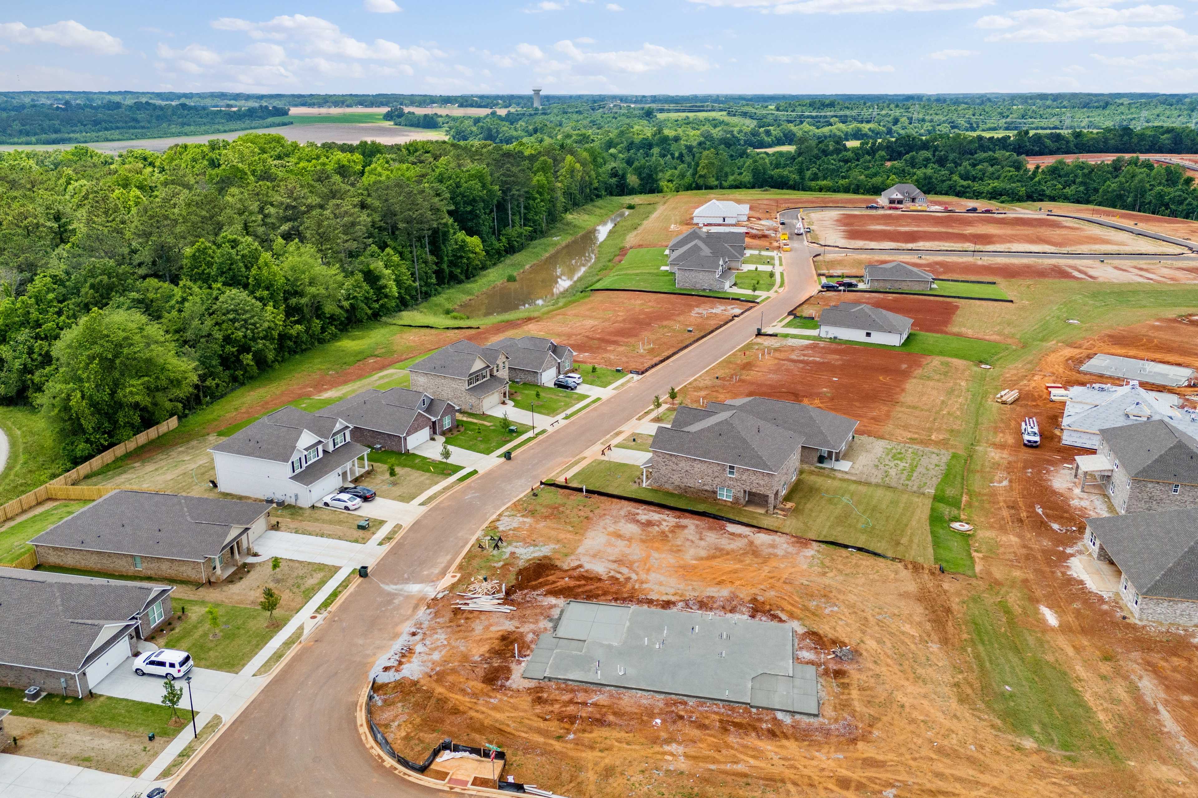 Aerial drone view of Creekside new homes under construction in Harvest Alabama by Davidson Homes with wooded fields and dirt roads