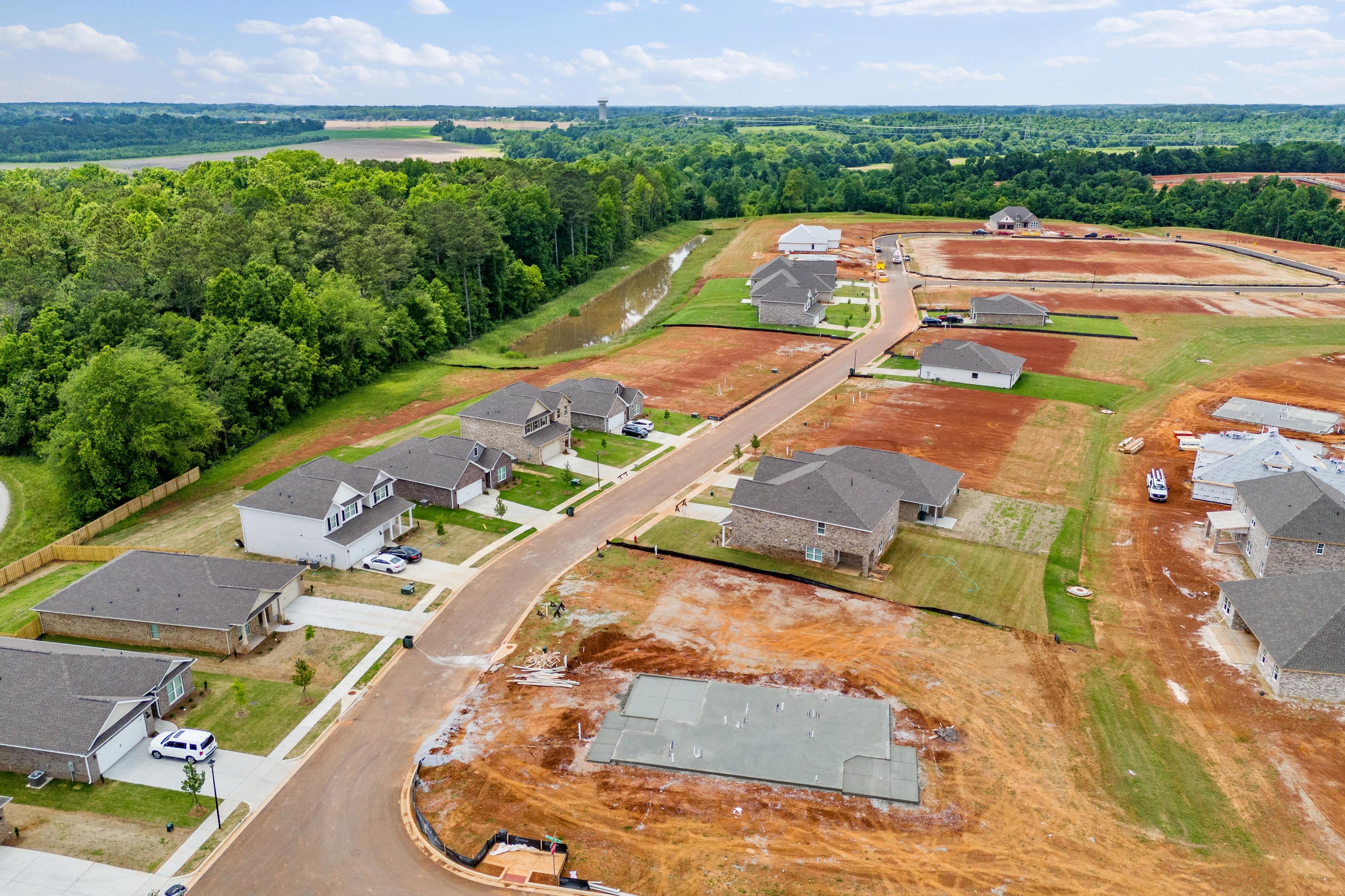 Aerial drone view of Creekside new homes under construction in Harvest Alabama by Davidson Homes with wooded fields and dirt roads