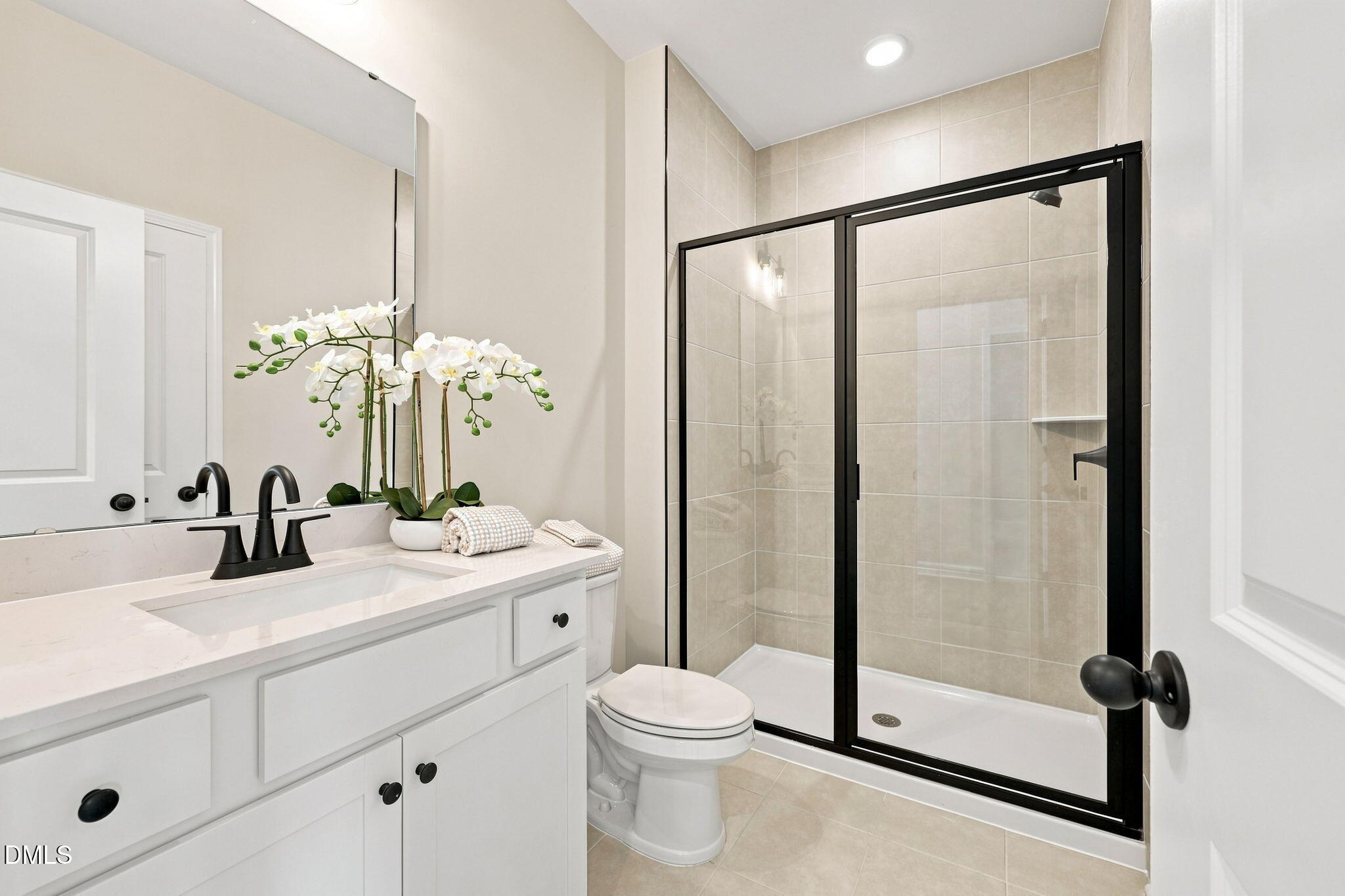 Modern bathroom with white vanity, black hardware, and glass-enclosed shower in The Harris C by Davidson Homes, Knightdale.