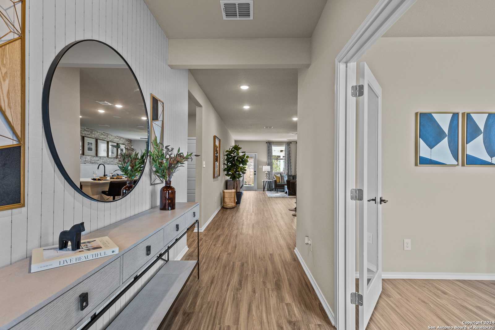 Elegant entryway hallway with round mirror, console table, vase, and hardwood floors in Davidson Homes The Douglas F, Bricewood, San Antonio