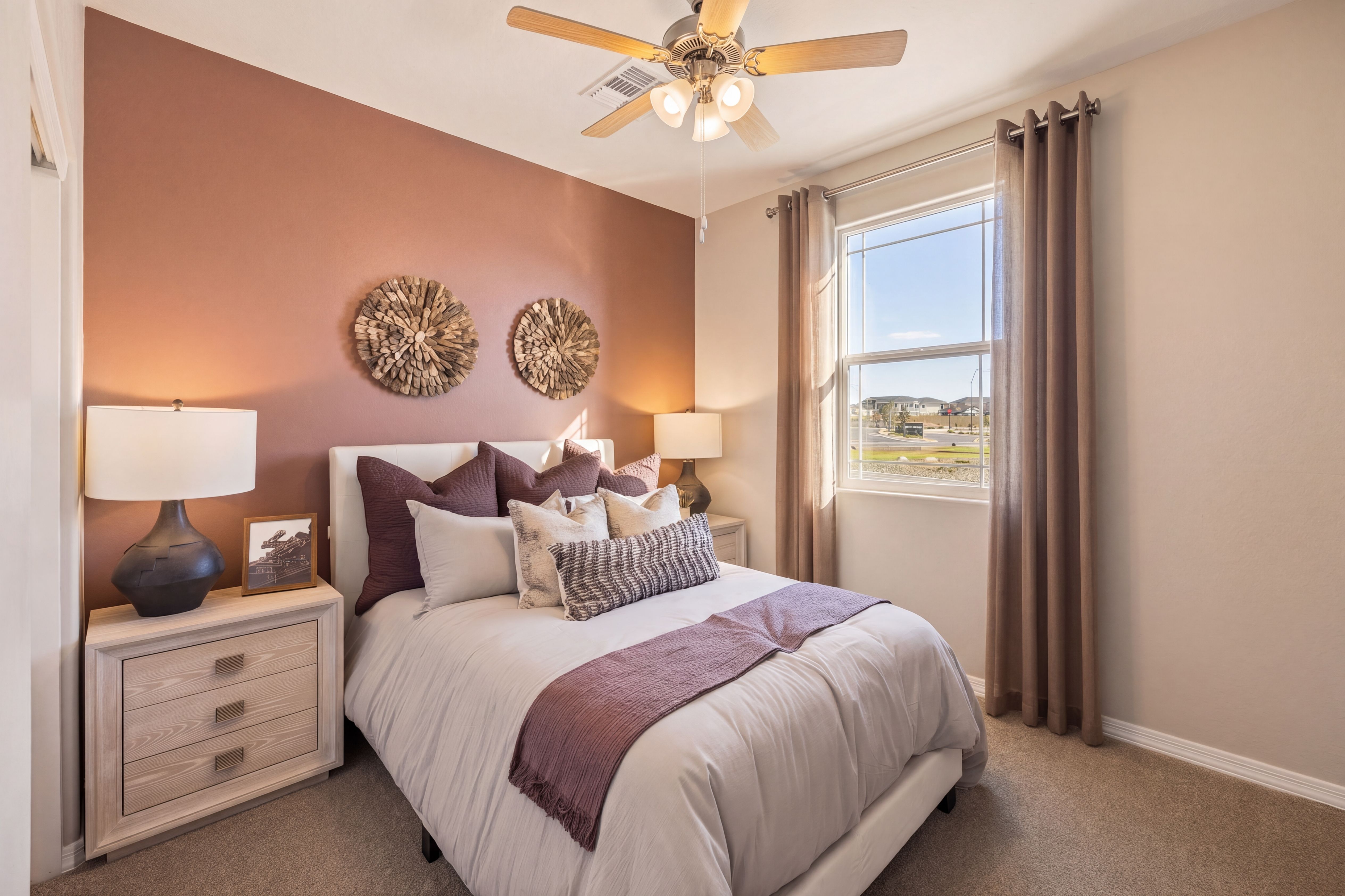 Cozy bedroom with queen bed, purple pillows, woven wall art, ceiling fan, and window view at Senator Cottages in Prescott AZ