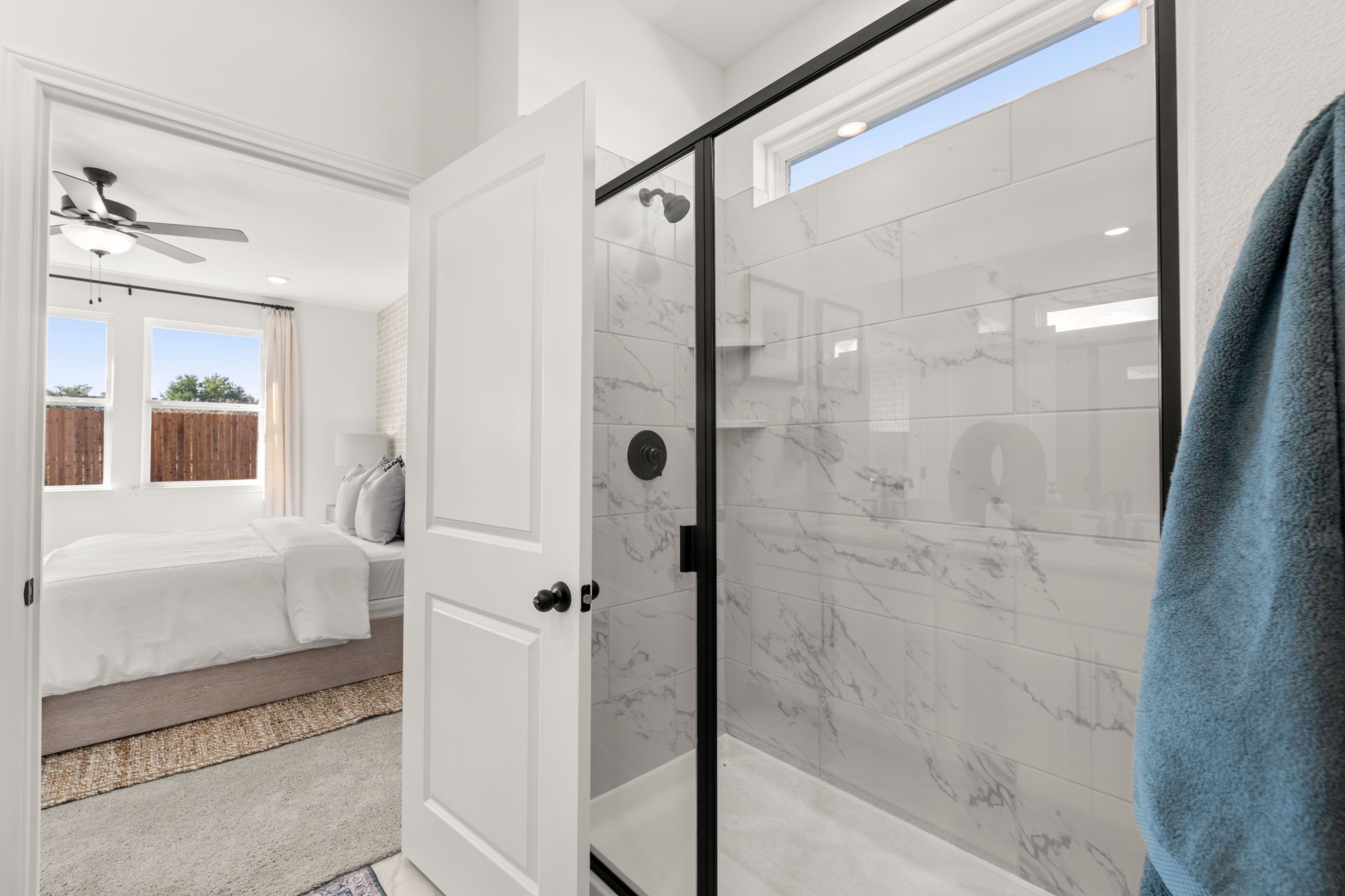 Spacious master bathroom in The Laurel with frameless glass walk-in shower, marble tiles, and open bedroom view