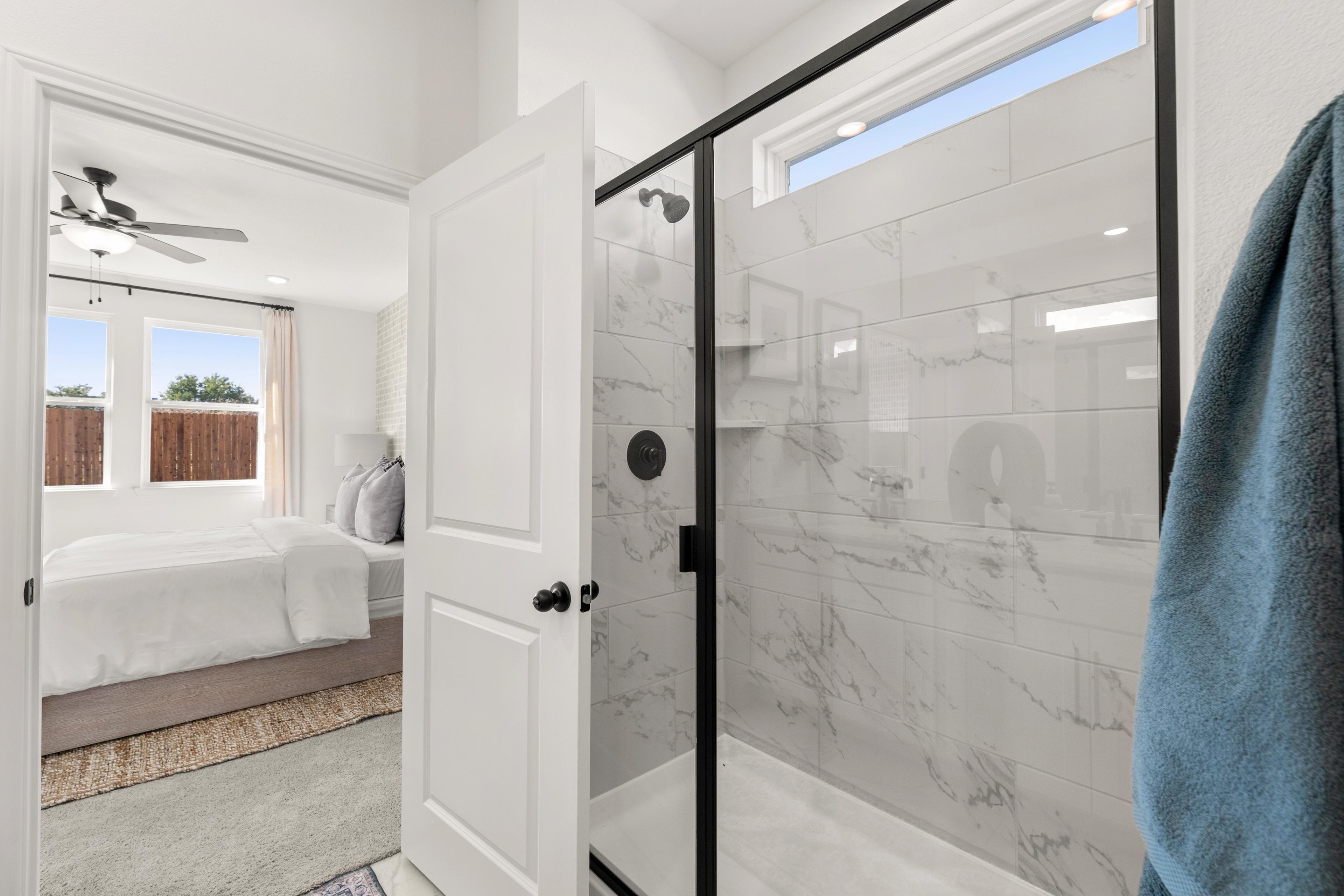 Master bathroom in The Laurel G Davidson Homes design featuring frameless glass shower, marble tile walls, and open bedroom with king bed