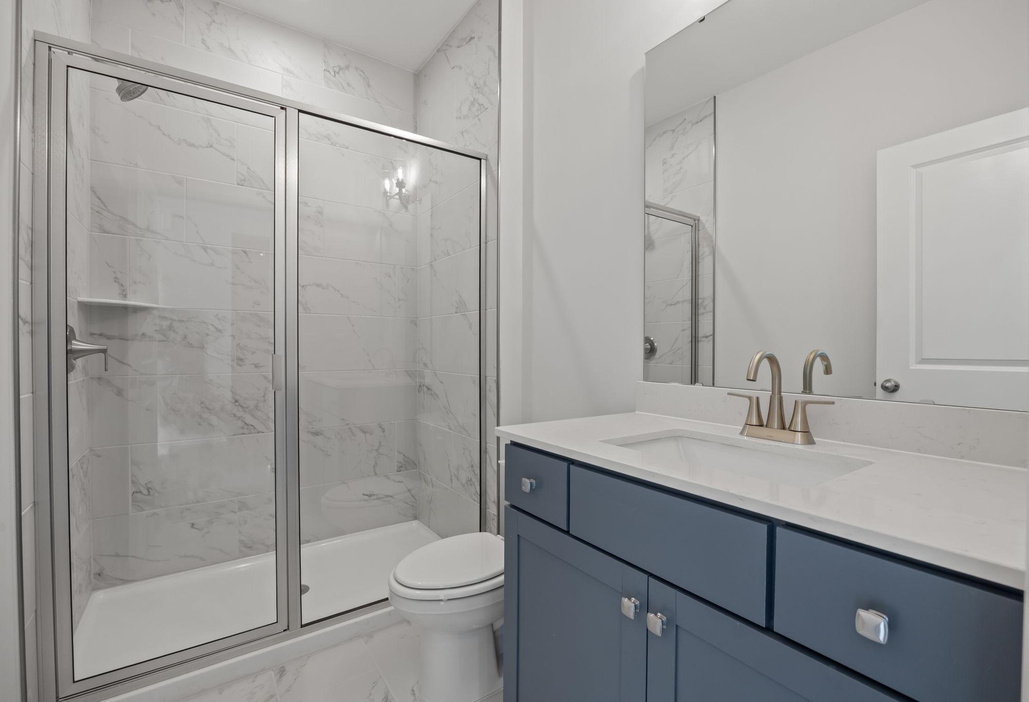 Modern bathroom in The Ashport C featuring a blue vanity, marble-style tile shower, and contemporary fixtures.