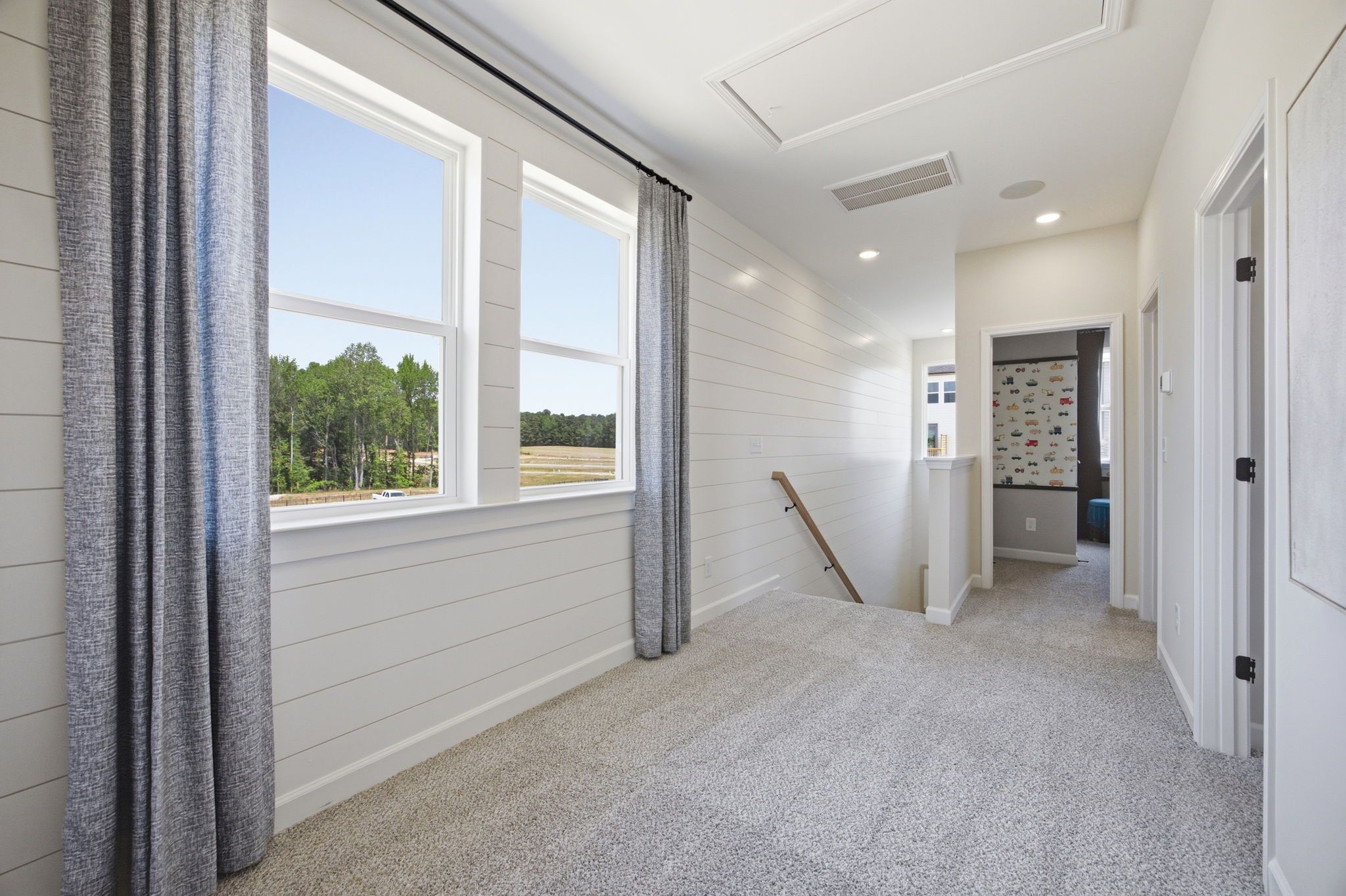 Bright upper-floor hallway in The Burke C home featuring white shiplap walls, carpeted flooring, and large windows.