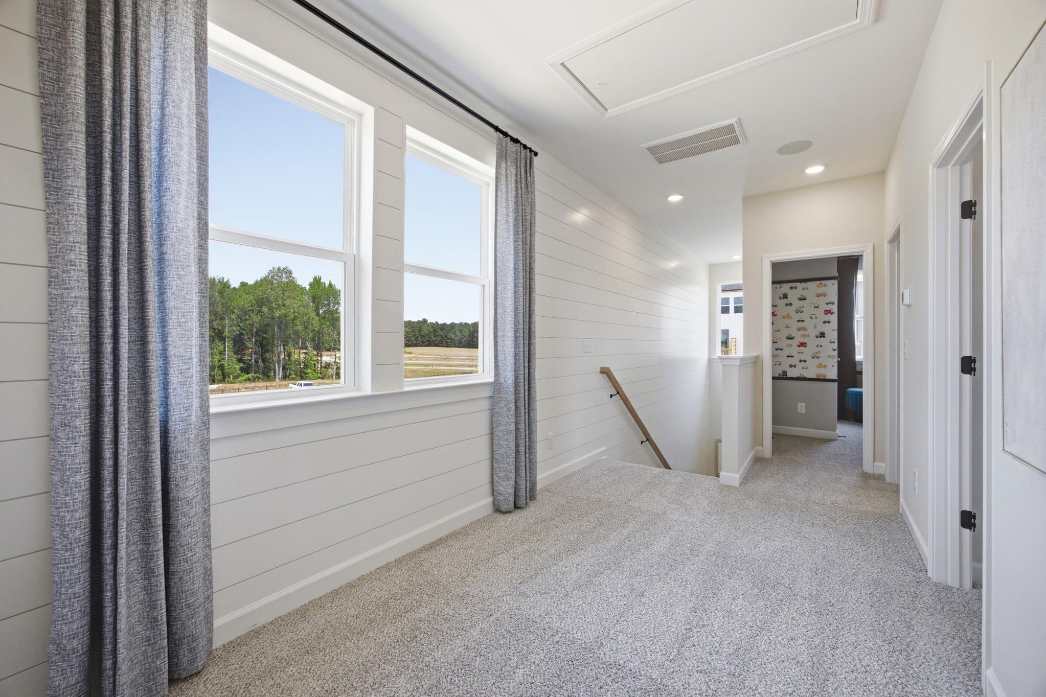 Bright upper-floor hallway in The Burke C home featuring white shiplap walls, carpeted flooring, and large windows.