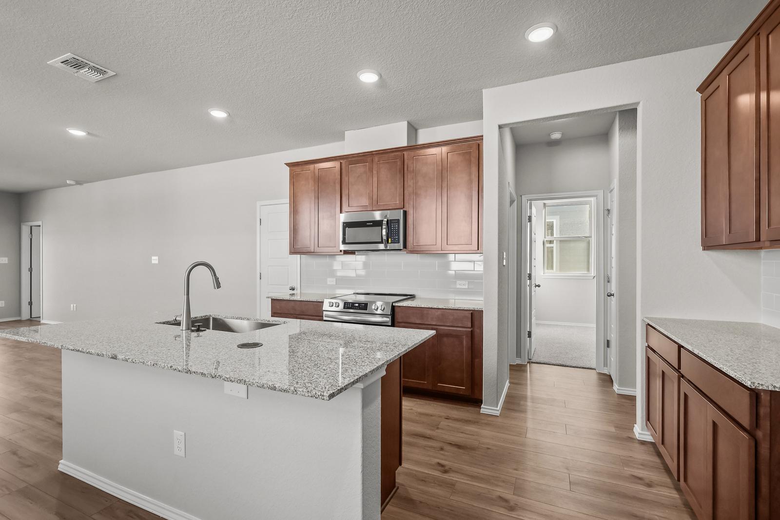 Open-concept kitchen in The Arroyo featuring granite countertops, wood cabinetry, and stainless steel appliances.