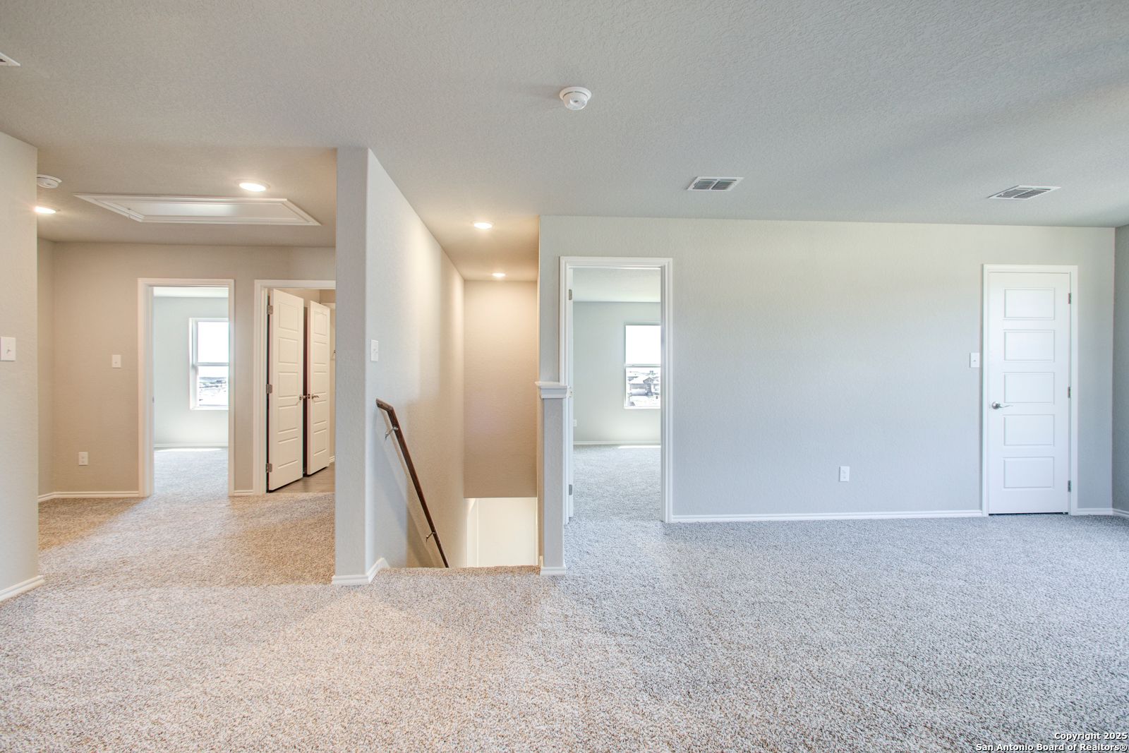 Spacious upstairs hallway with carpeted floors, bedroom doors, and staircase in 4-bedroom Davidson Homes The Douglas G, San Antonio, Texas
