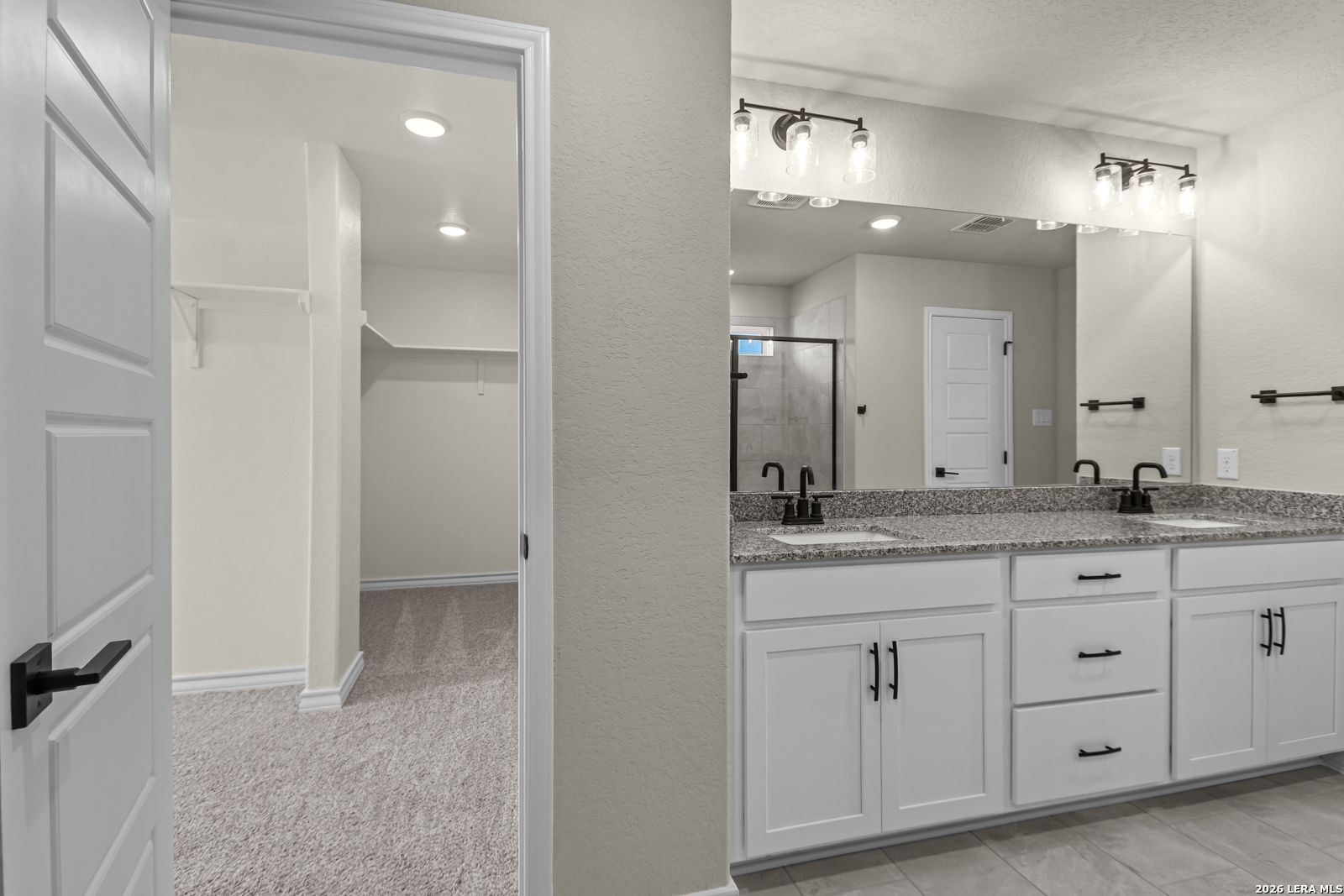 Primary bathroom with dual vanity, granite countertops, and walk-in closet in The Danbury H, Potranco Oaks, Castroville, TX.