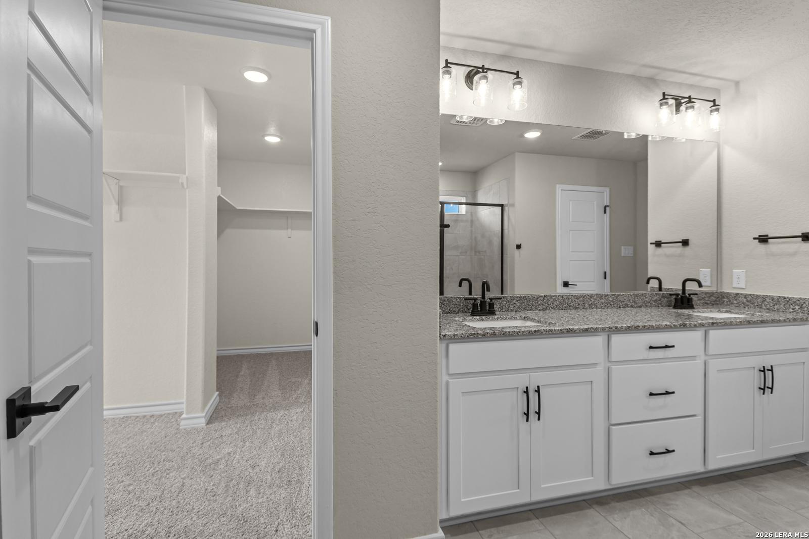 Primary bathroom with dual vanity, granite countertops, and walk-in closet in The Danbury H, Potranco Oaks, Castroville, TX.