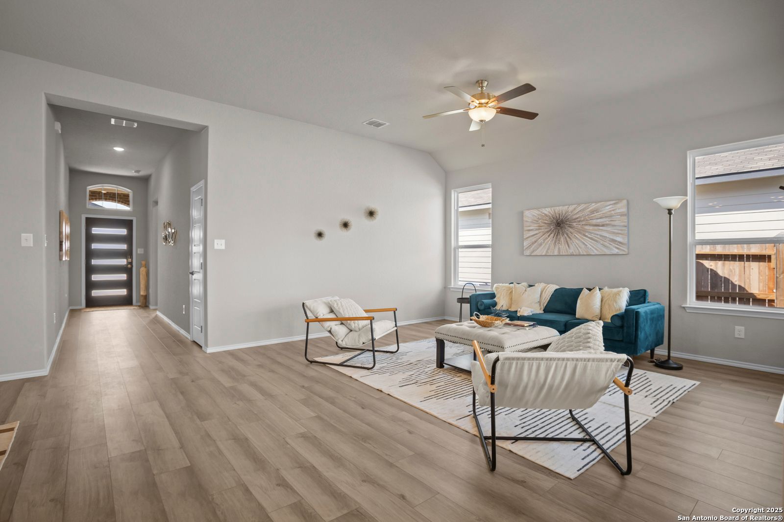 Modern living room with teal sofa, white armchairs, ceiling fan, and wood floors in Davidson Homes The Collin B, Seguin, Texas