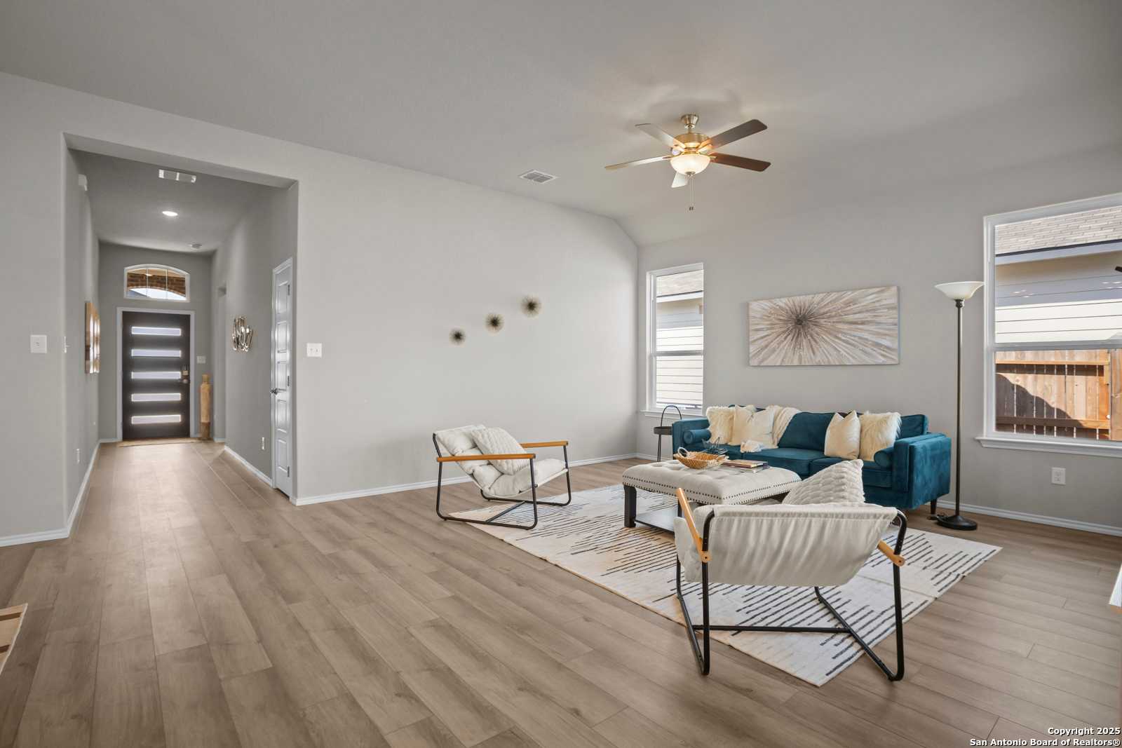 Modern living room with teal sofa, white armchairs, ceiling fan, and wood floors in Davidson Homes The Collin B, Seguin, Texas