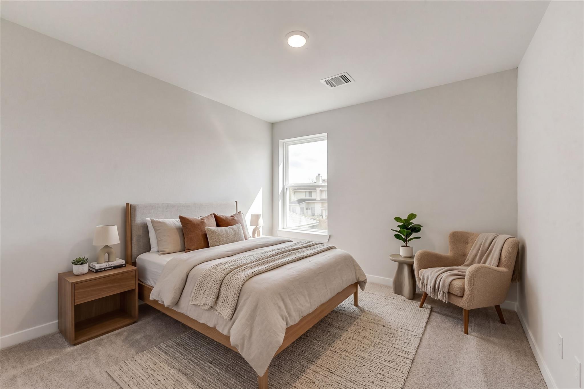 Serene neutral-toned bedroom with wooden bed, plush beige bedding, velvet armchair, potted plants, and large window in Davidson Homes The Brazos E, Dayton, Texas
