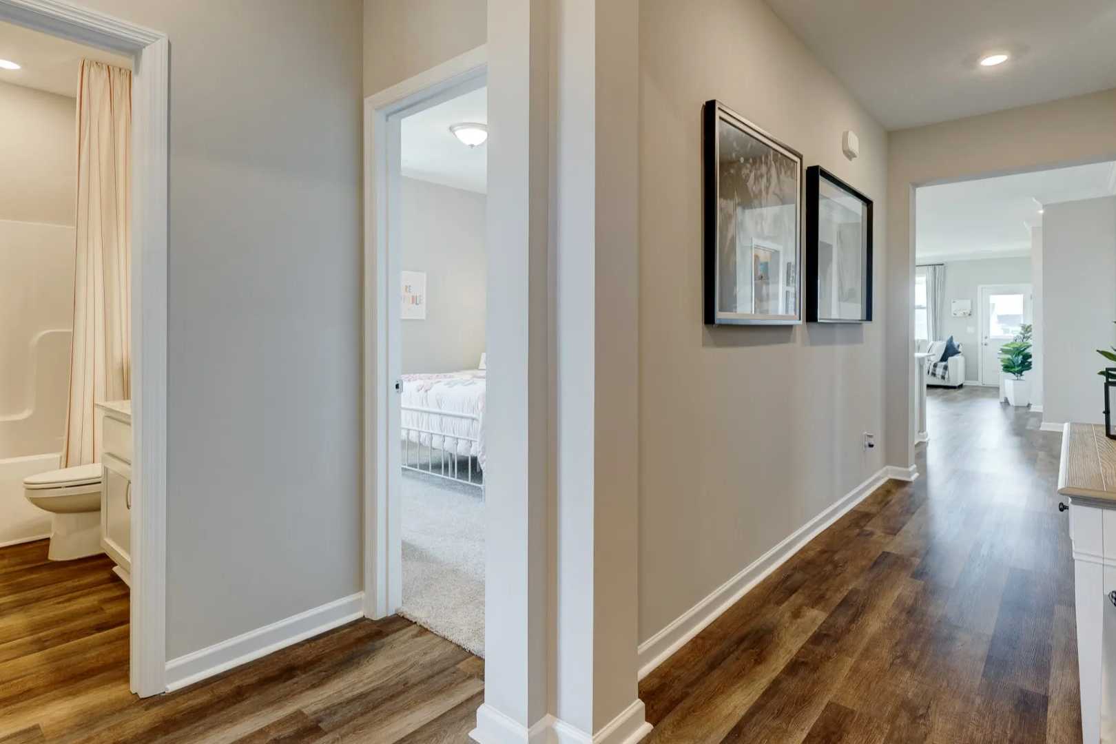 Spacious master bathroom and bedroom hallway in The Aurora B home design with neutral walls, hardwood floors, and tub