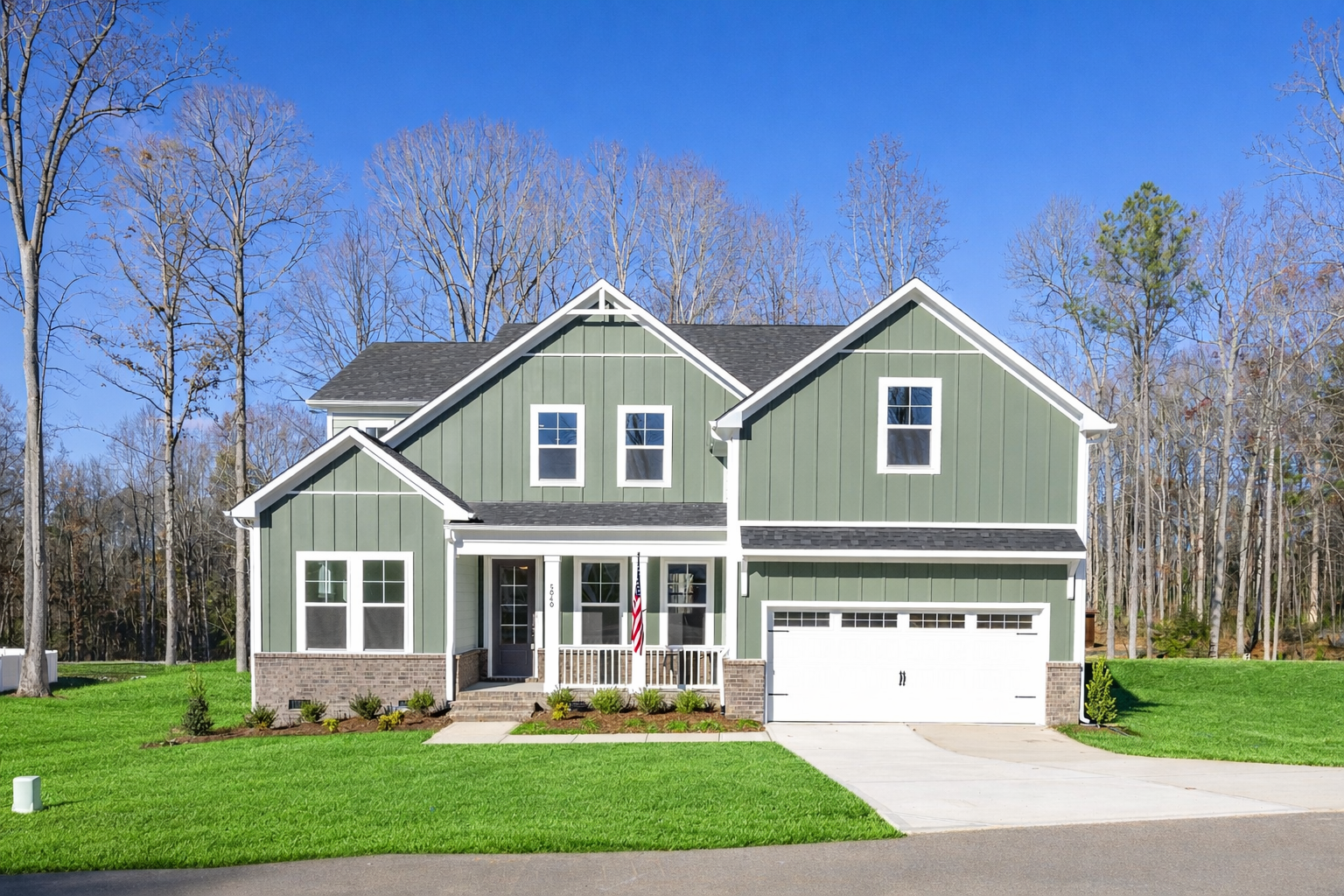 Sage green Craftsman home exterior at Ashland in Apex NC with covered front porch, two-car garage, and wooded backdrop