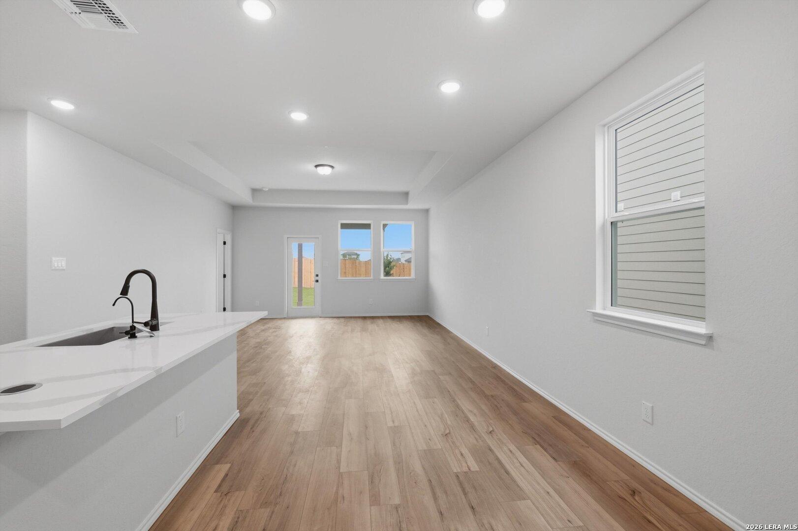 Modern white quartz kitchen island with black faucet and hardwood floors in open living area of The Blanco C home, Agave, San Antonio, Texas